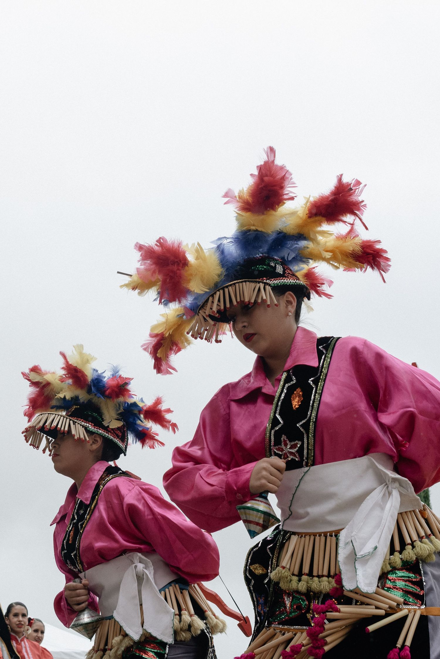 Dancers in pink shirts and feathered headdresses perform traditional Native American dances at a cultural festival.
