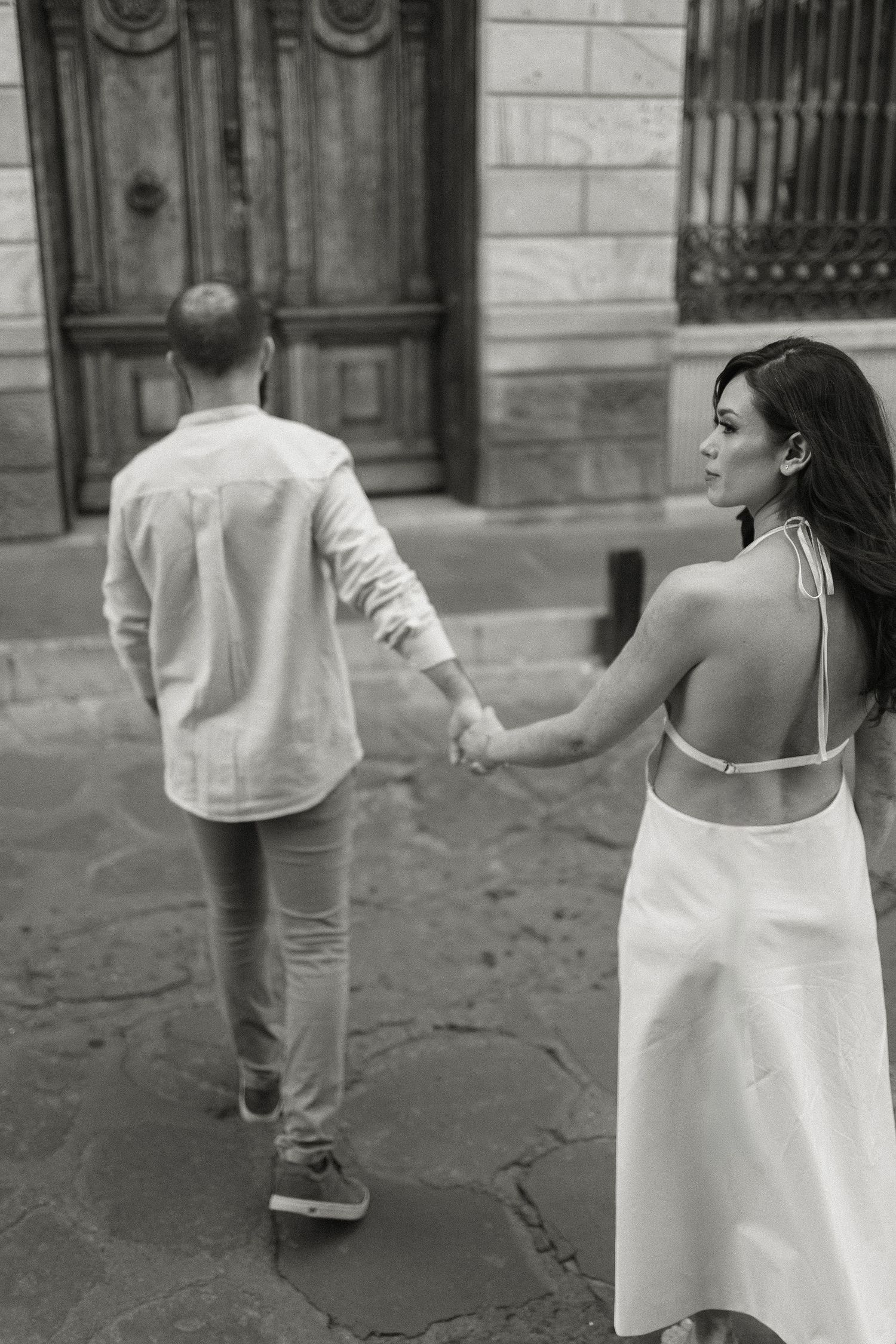Black and white photo series showing couple in white clothing walking together on a cobblestone street.