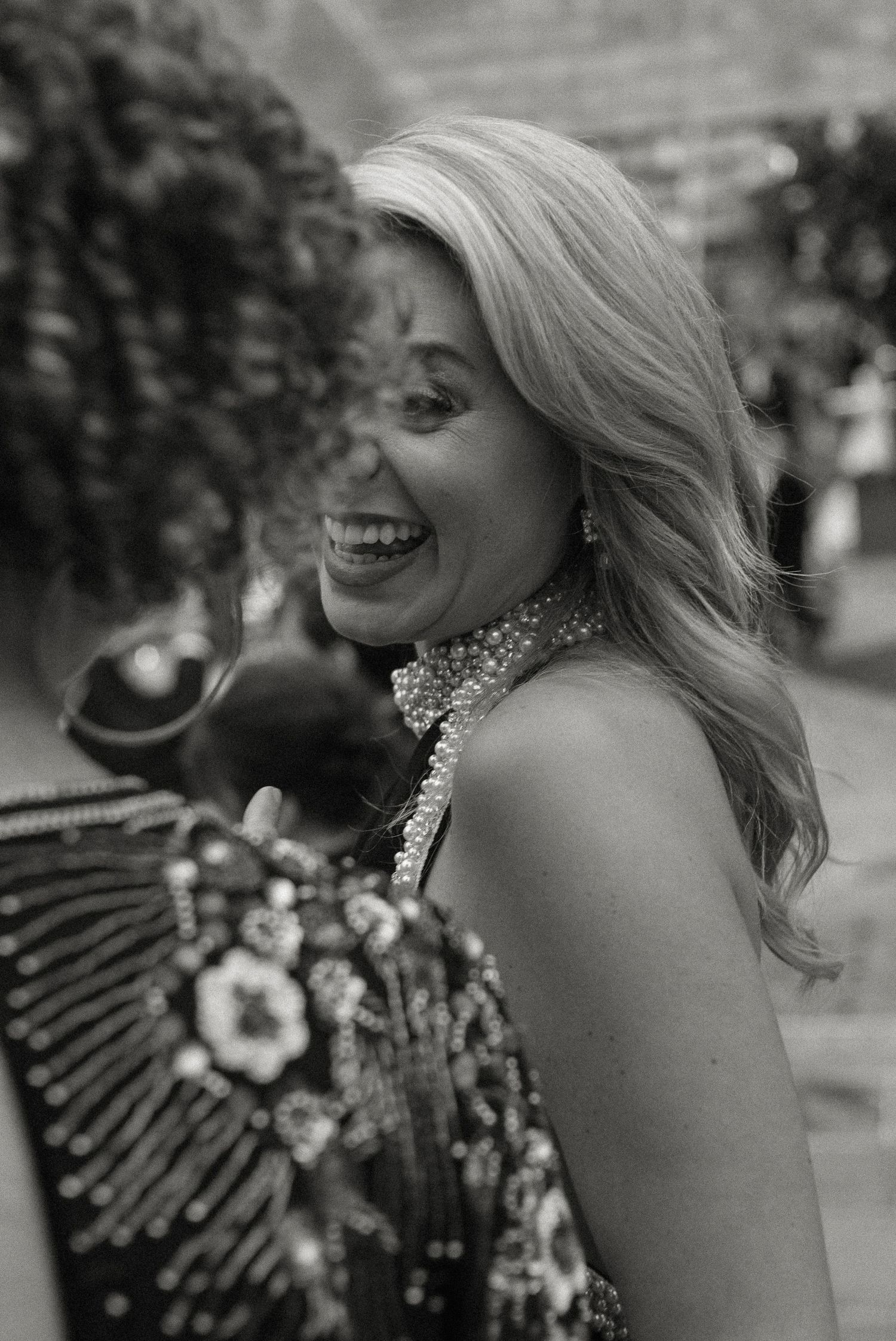 A black and white candid portrait of a joyful person in a sparkly high-neck dress with blonde wavy hair.