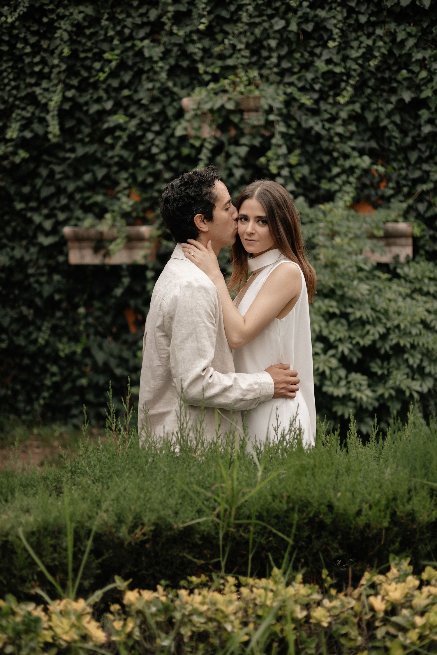 Romantic garden scene with couple embracing among lush greenery and flowers.