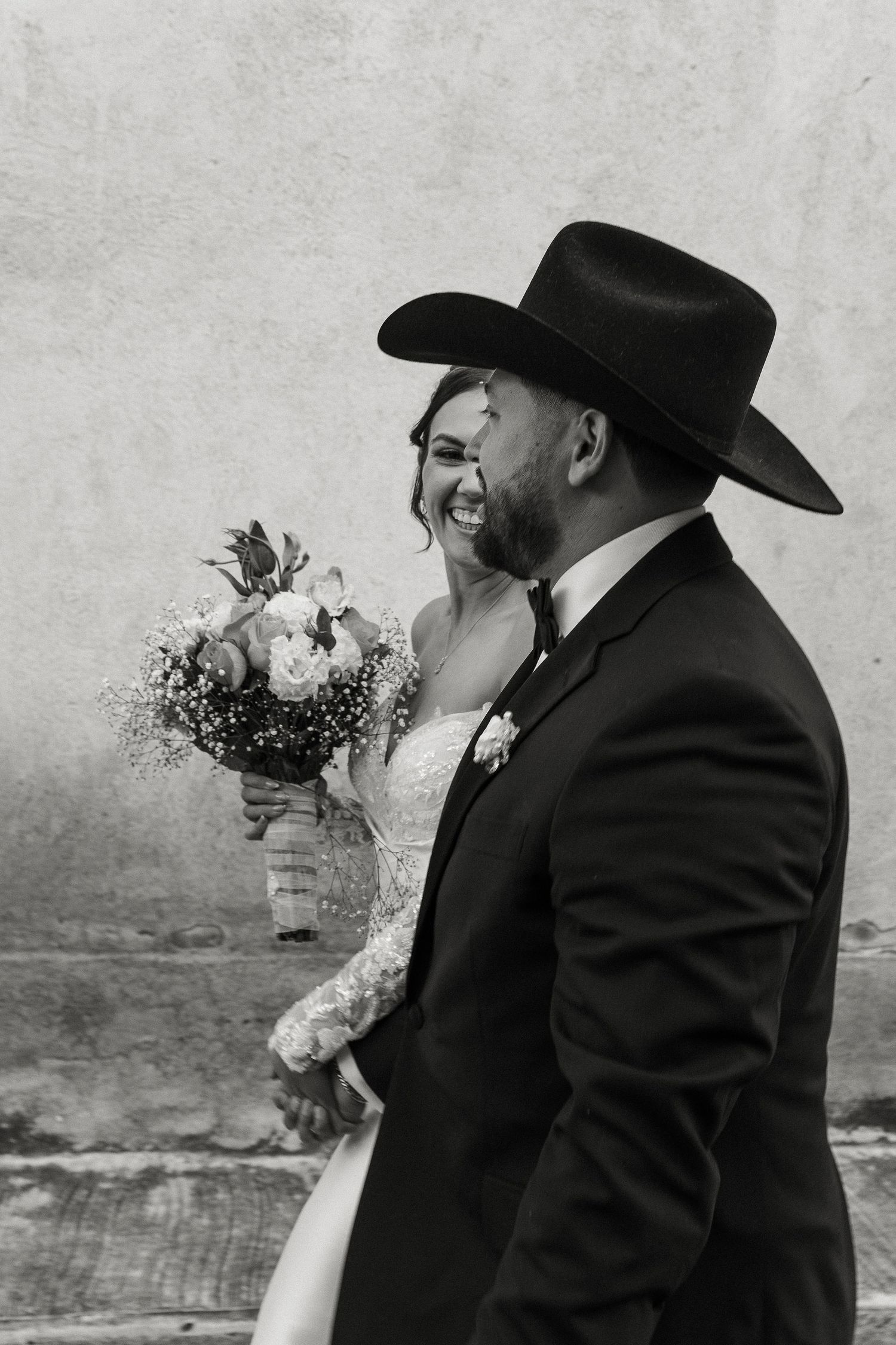 A romantic wedding sequence showing a couple in black attire sharing tender kisses against a textured gray wall.