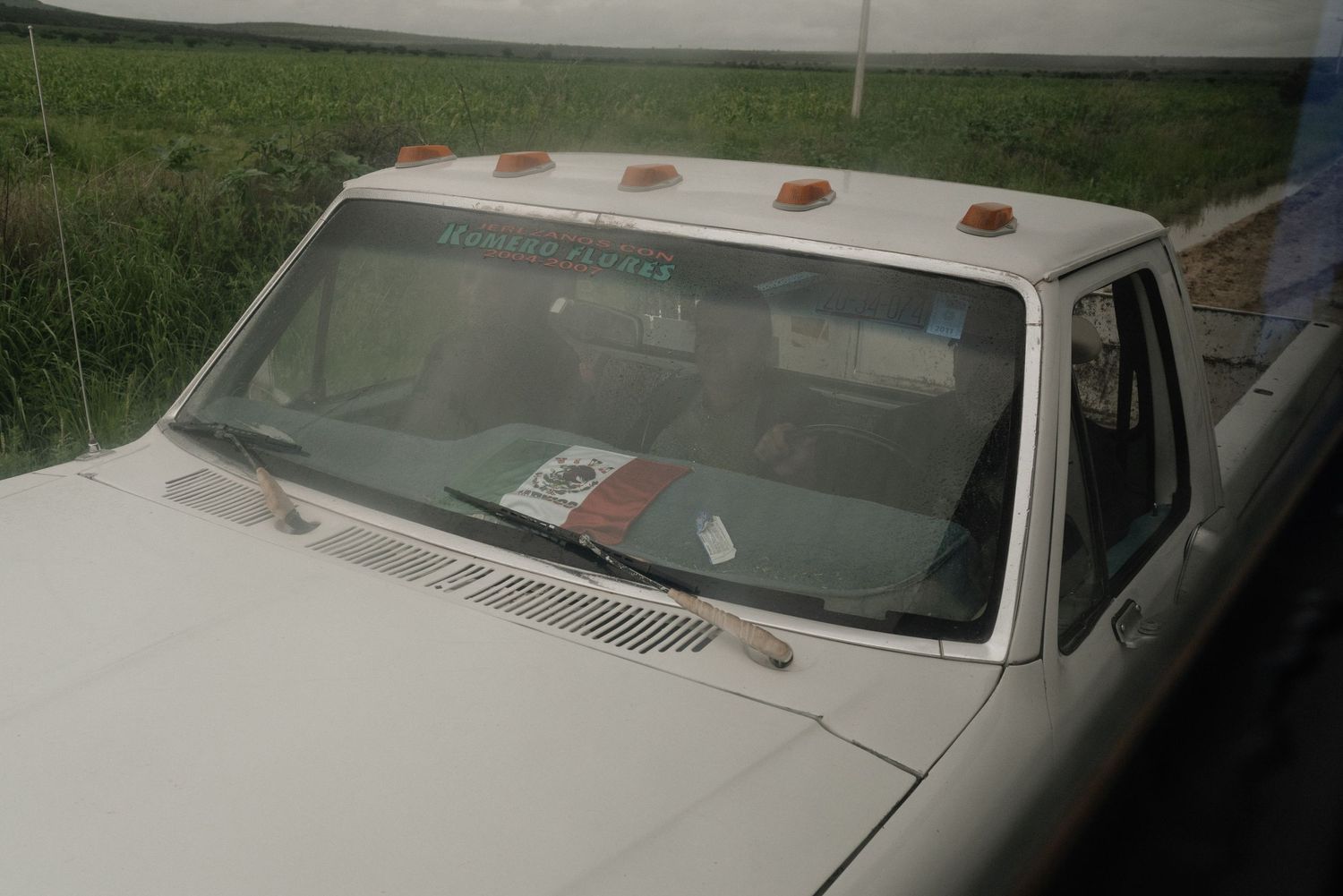 A vintage white car with marker lights on its roof viewed from the front windshield angle.