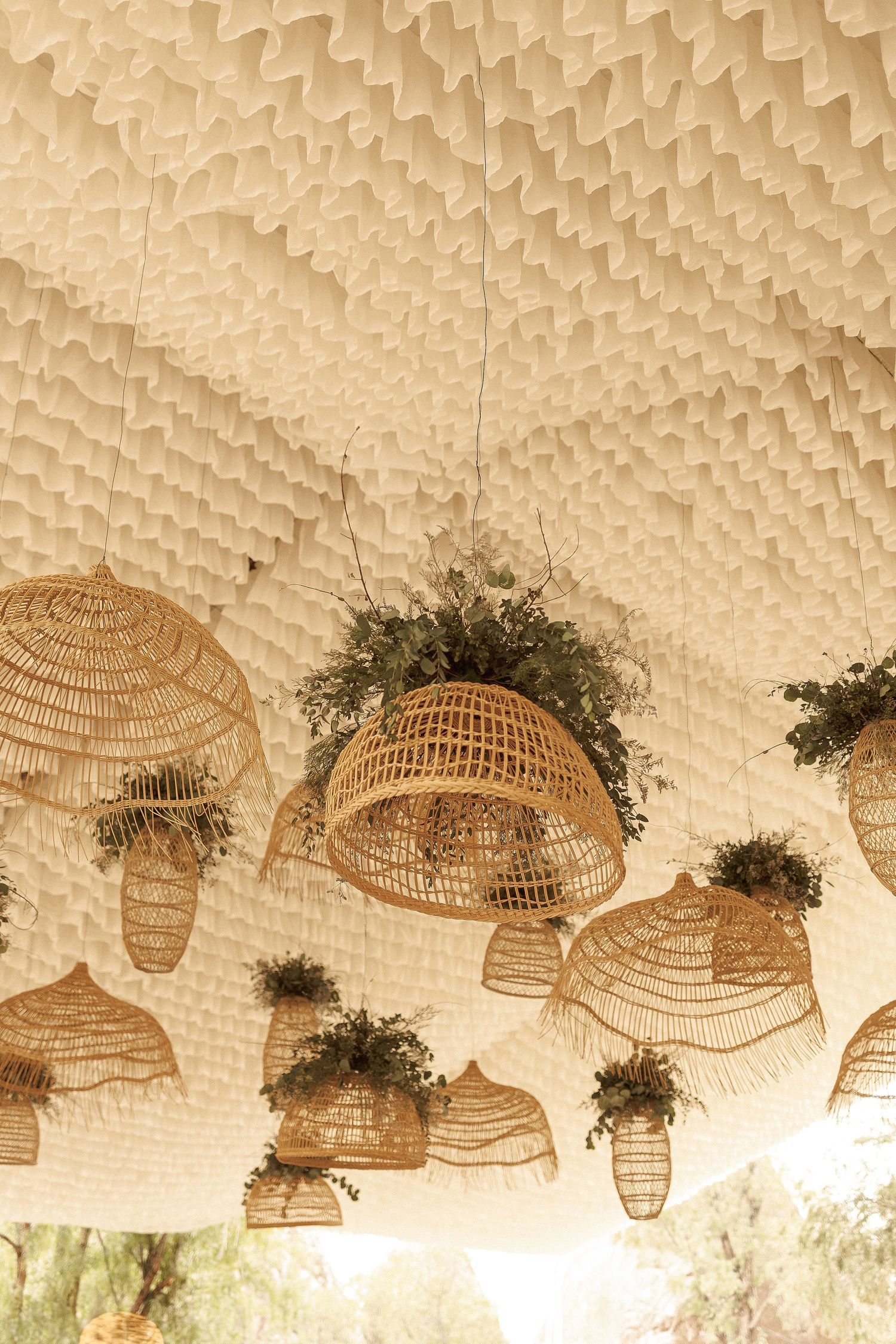 Rustic woven rattan basket lampshades with greenery hanging from a textured ceiling create a bohemian wedding decor.