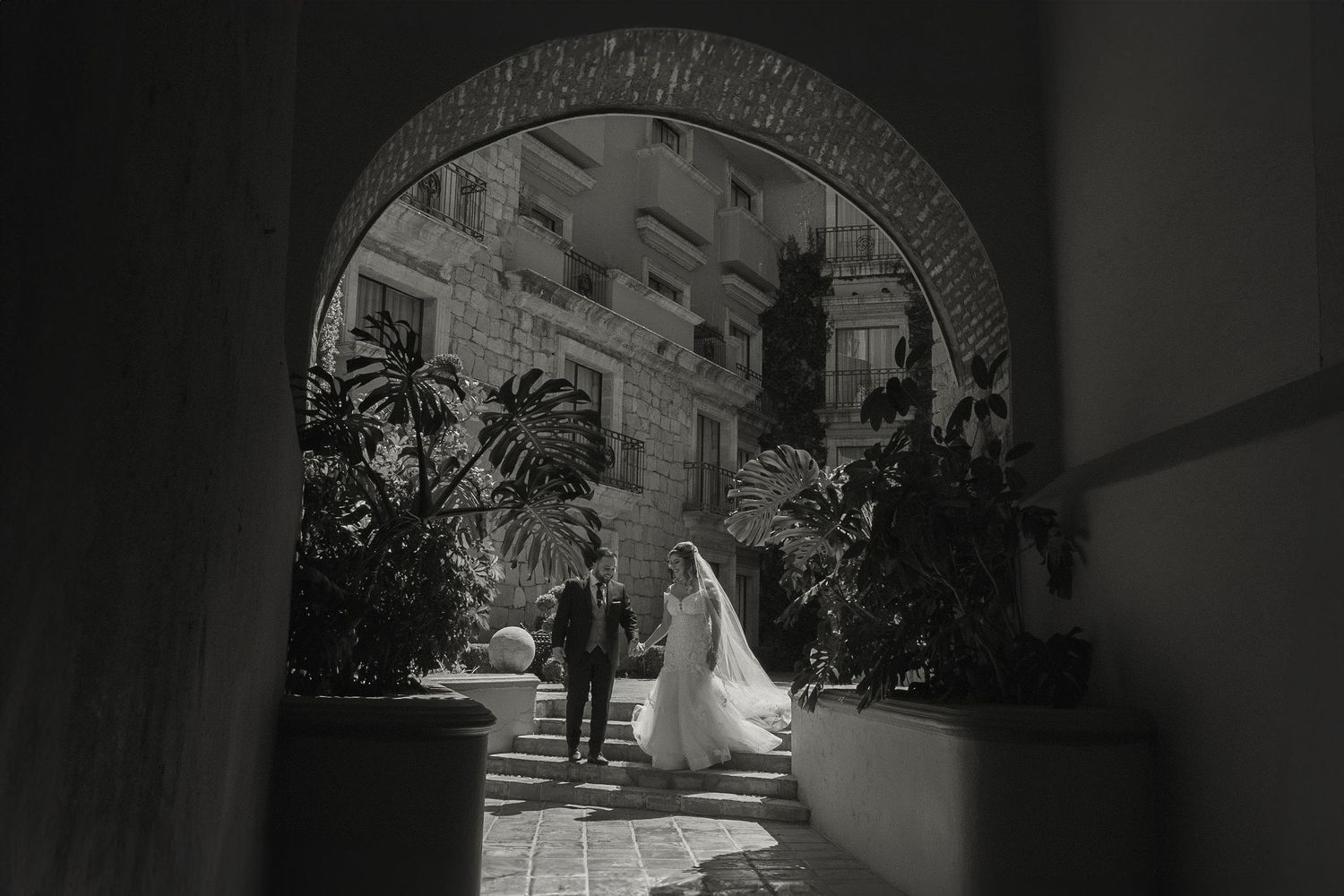 Sunlight streams through stone archways in a historic Spanish colonial courtyard.