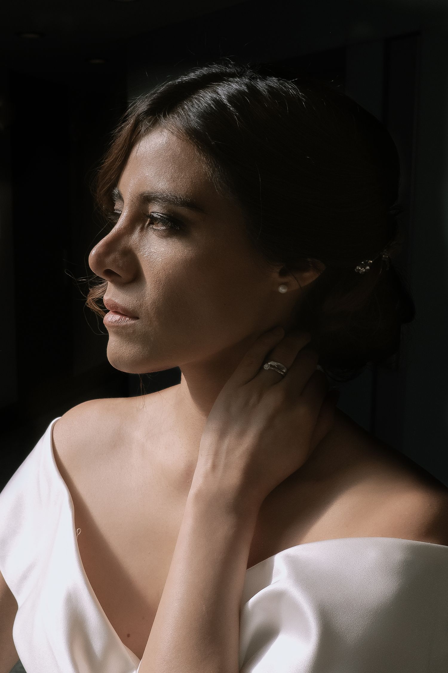 Side profile portrait in dramatic lighting showcasing elegant bridal jewelry and an off-shoulder white dress.