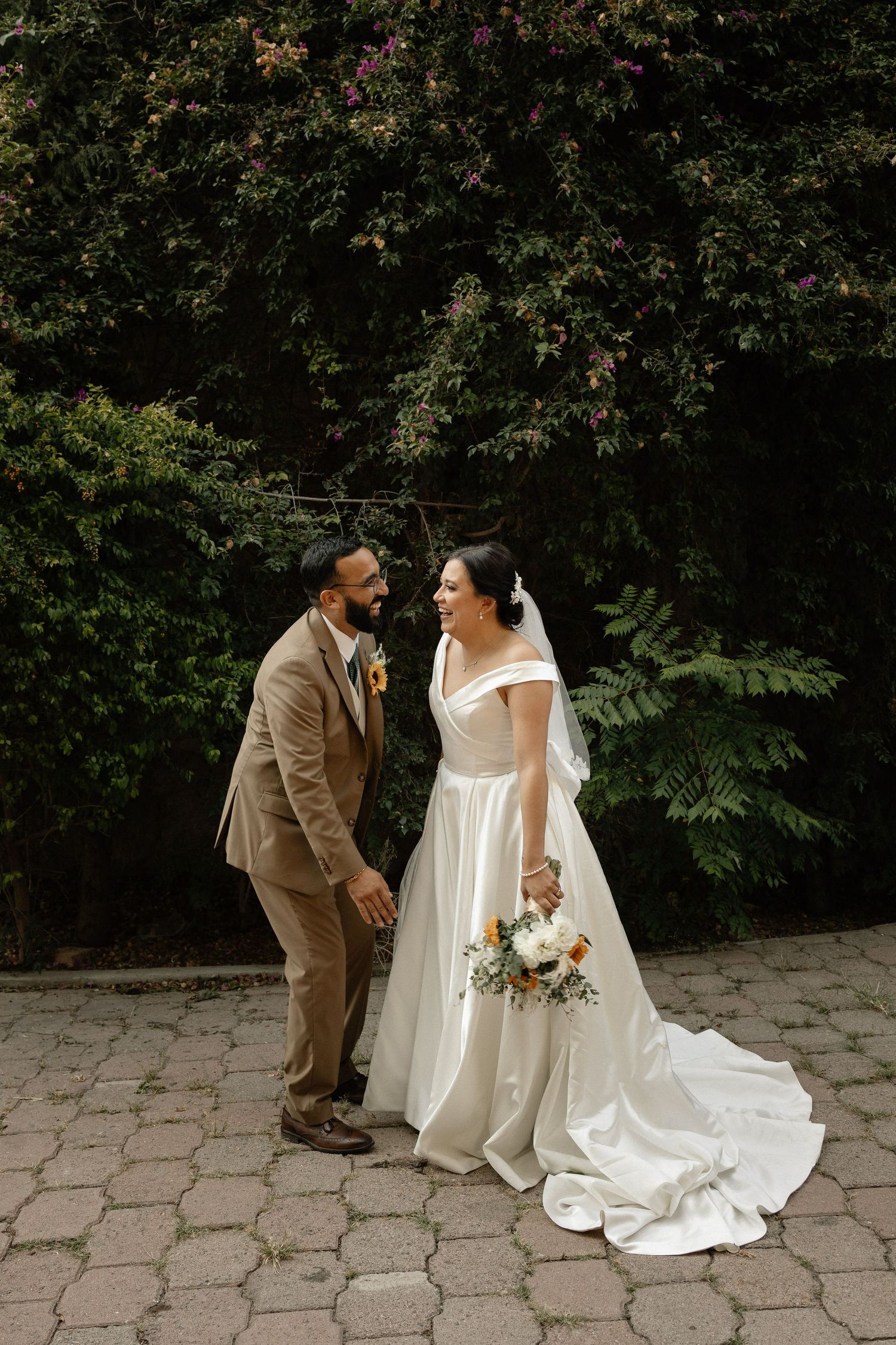 A wedding couple shares an intimate moment on stone pavers surrounded by lush greenery.