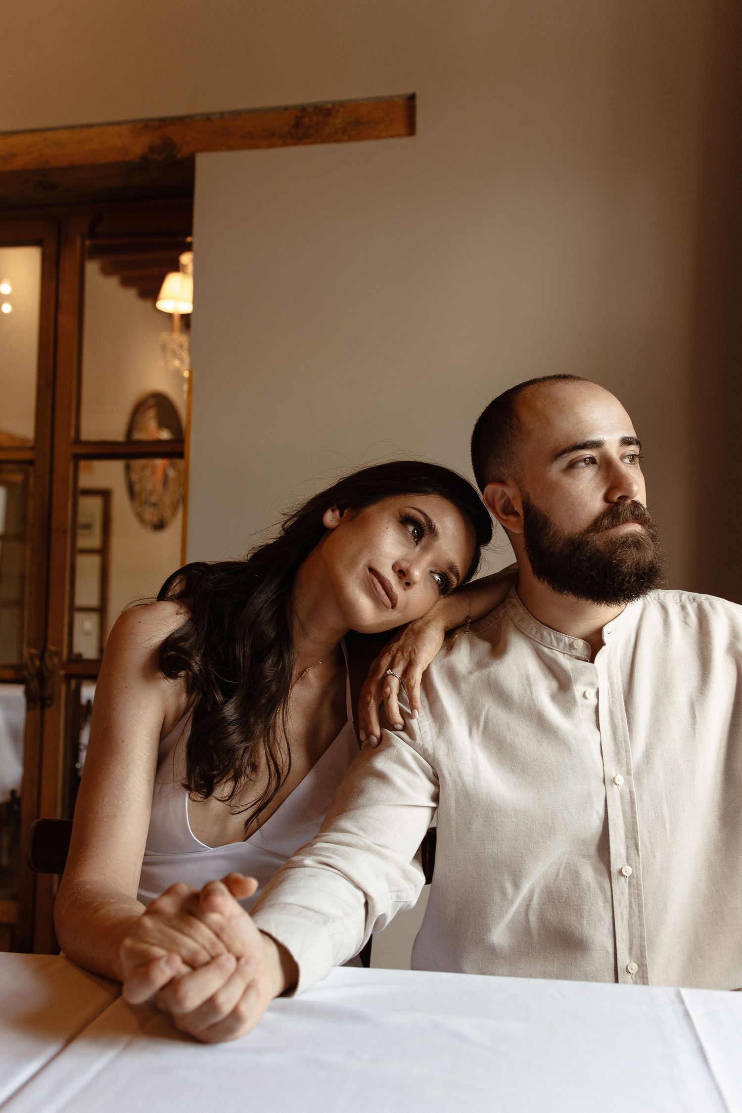 A couple sits together at a table in a warmly lit interior space, sharing an intimate moment.