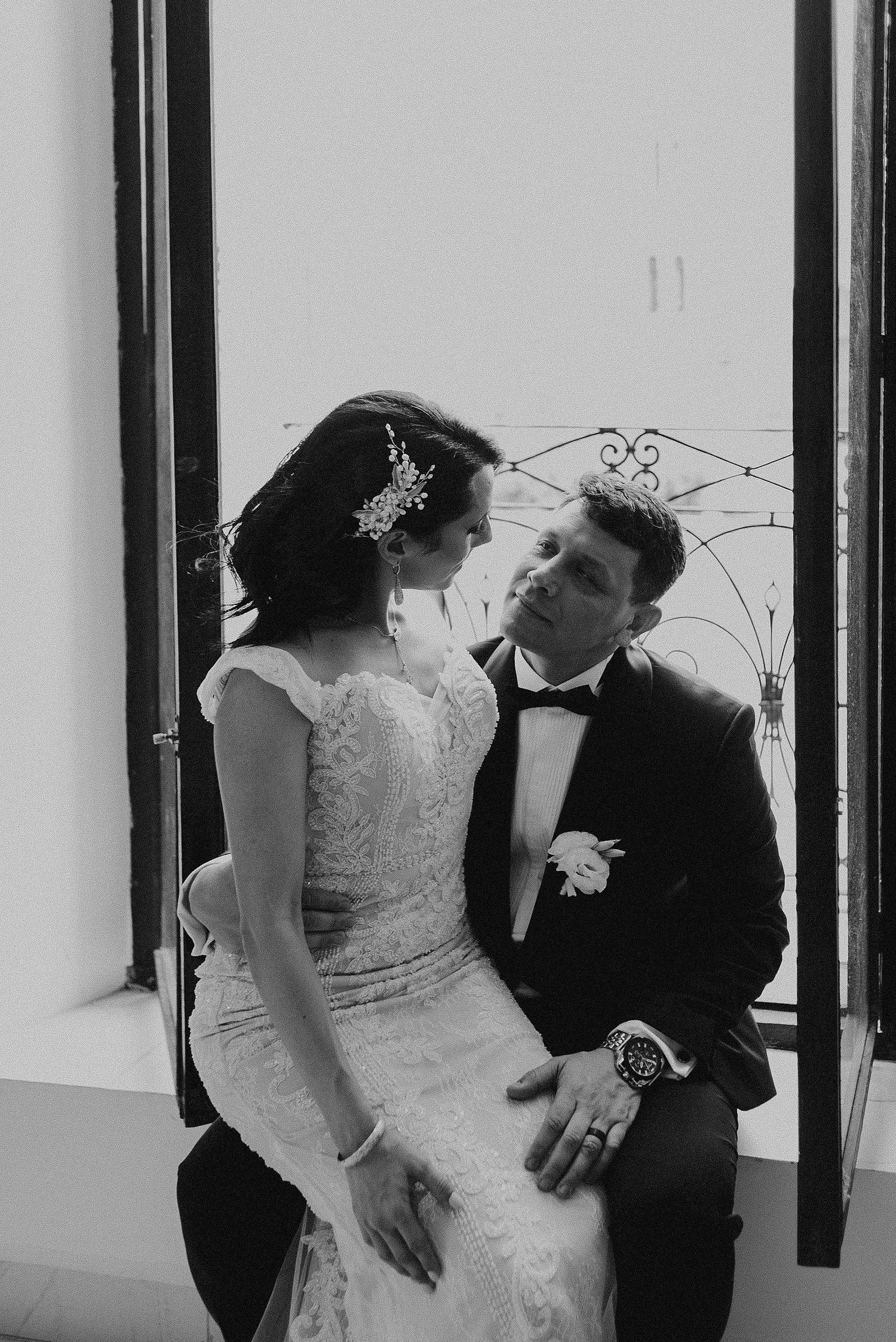 Black and white intimate portrait by window in formal attire.
