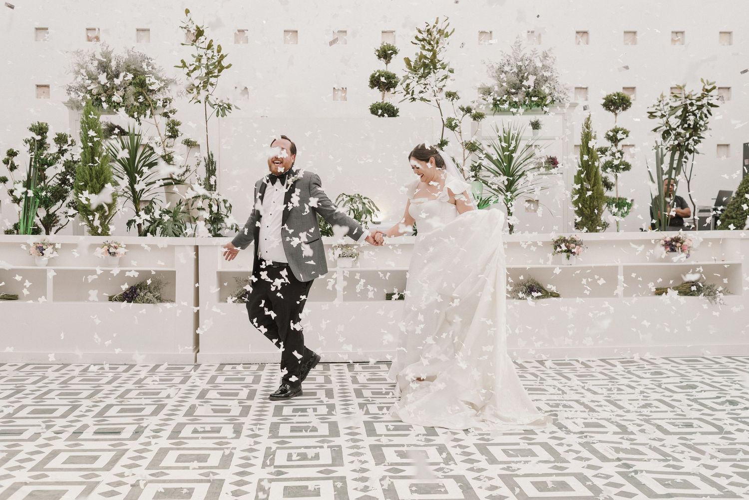 A couple playfully running through a courtyard with white walls and climbing vines.