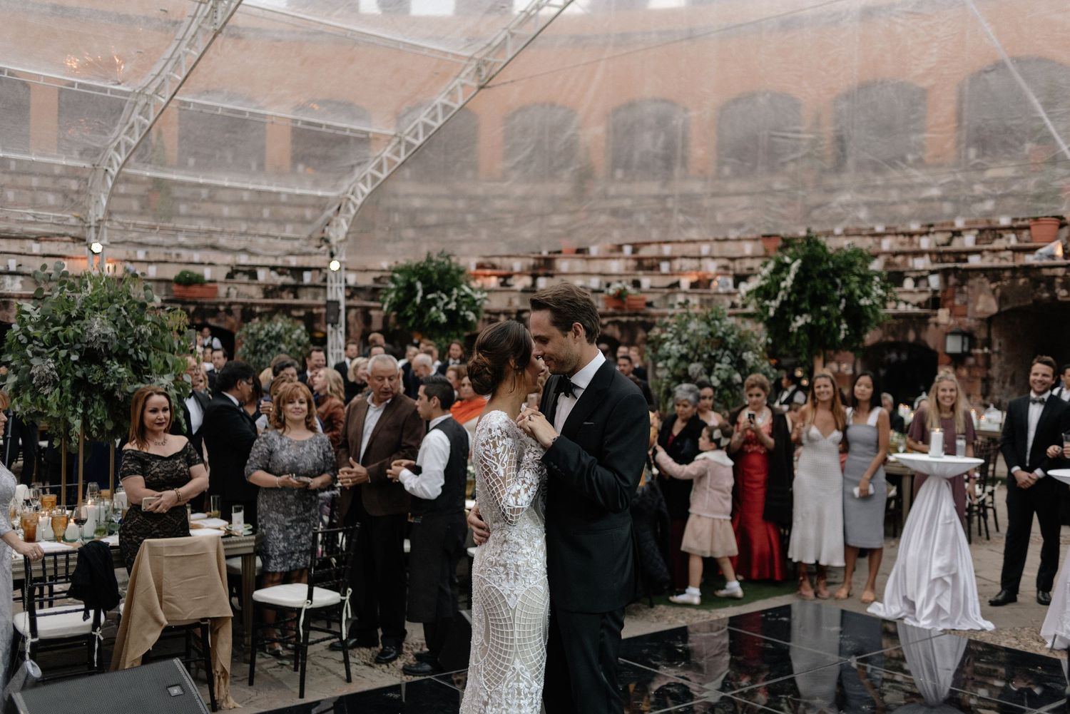 A couple dances during their first dance at an elegant indoor reception venue with guests watching from the sidelines.