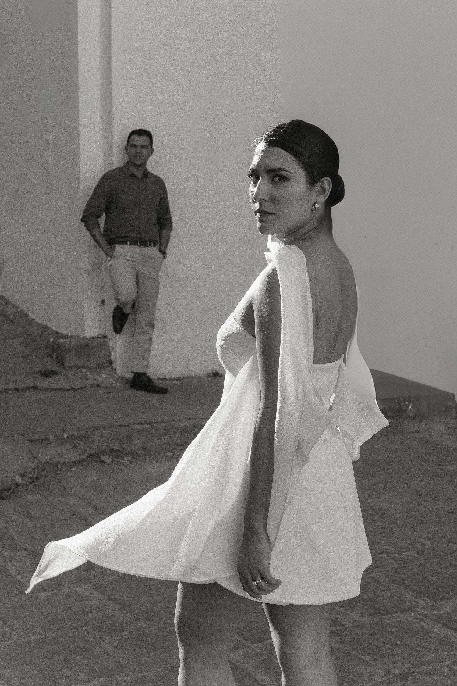 A series of black and white photos showing a figure in a white dress moving expressively against a plain wall.