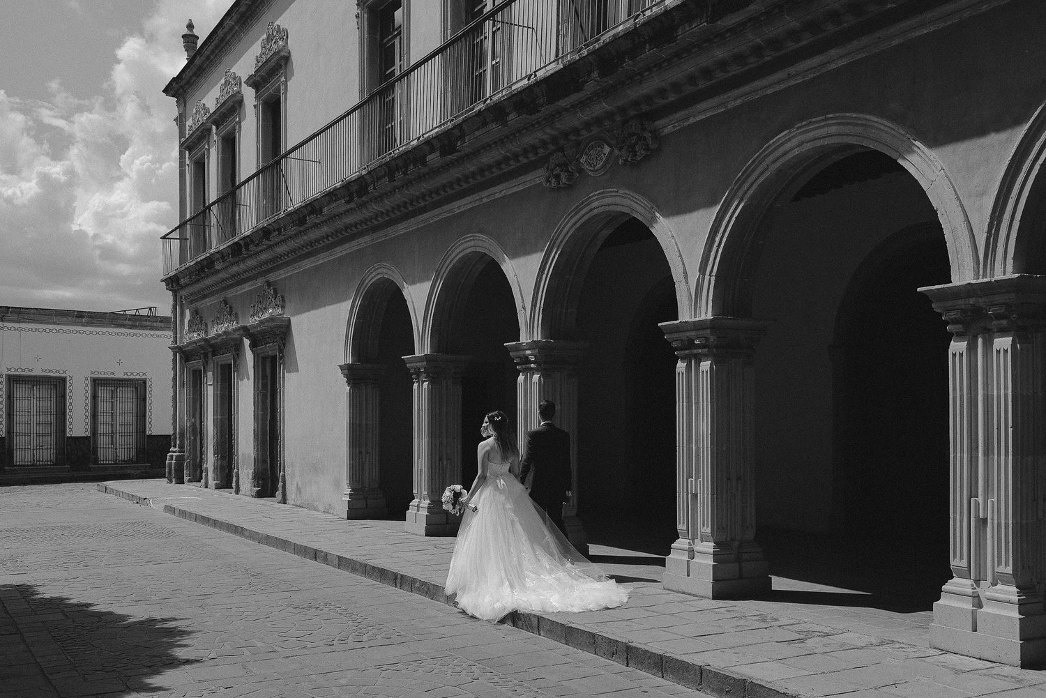Black and white architectural photo showing a row of arched columns and windows along a building facade.