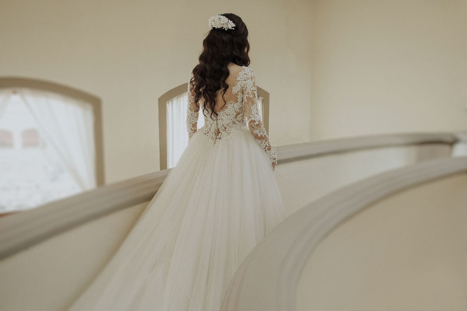 Elegant wedding dress with lace back detail and flowing tulle skirt photographed on curved staircase.