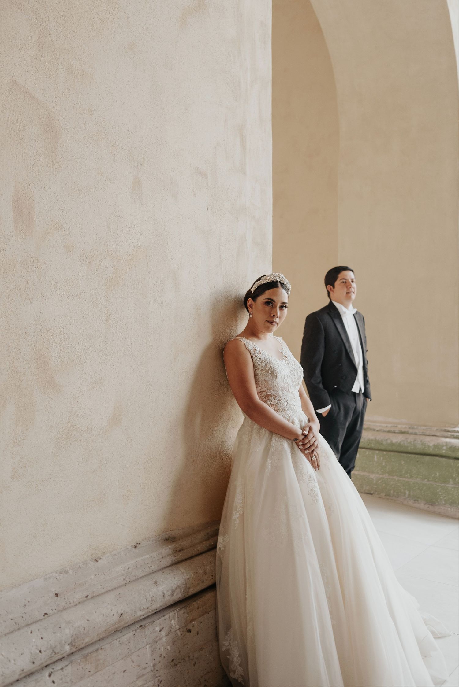 Wedding couple poses against minimalist white walls in an architectural setting.