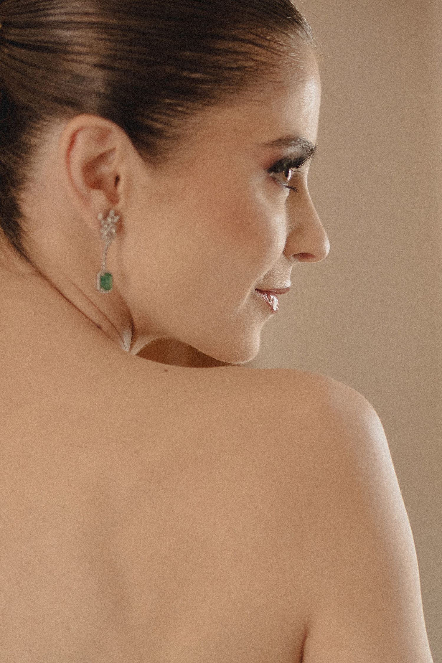 Close-up profile view of a woman's bare shoulder and neck wearing an elegant emerald earring.