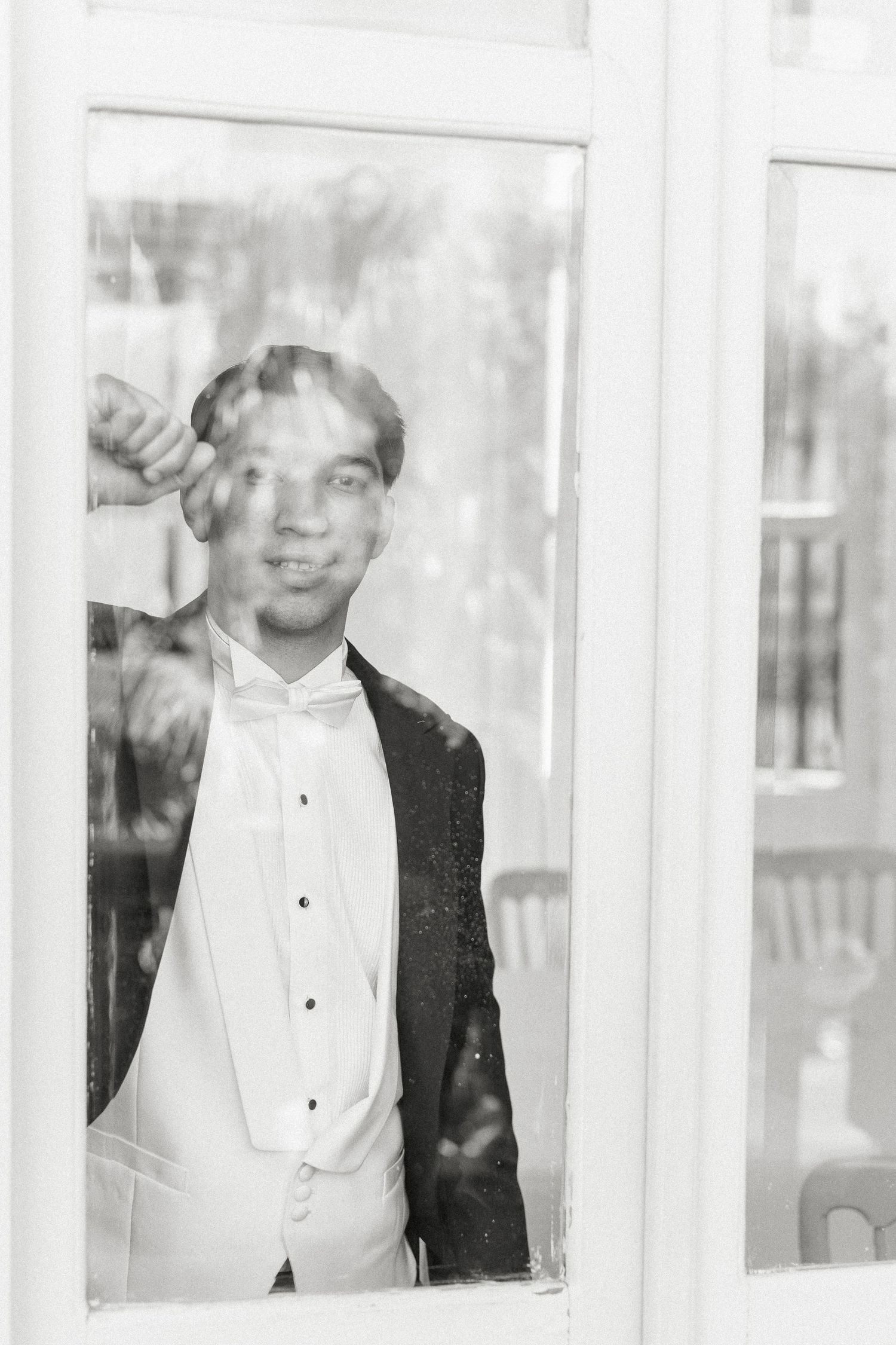 A black and white photograph of a person in formal attire visible through window panes.