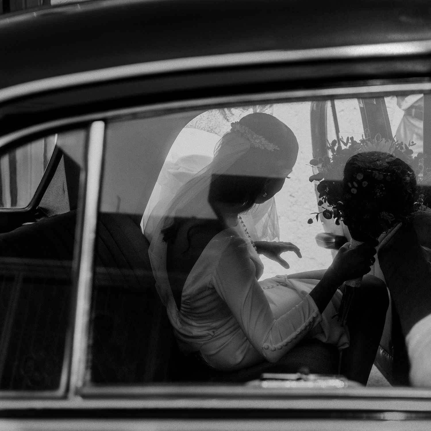 Silhouettes of a wedding couple seen through a car window in black and white.