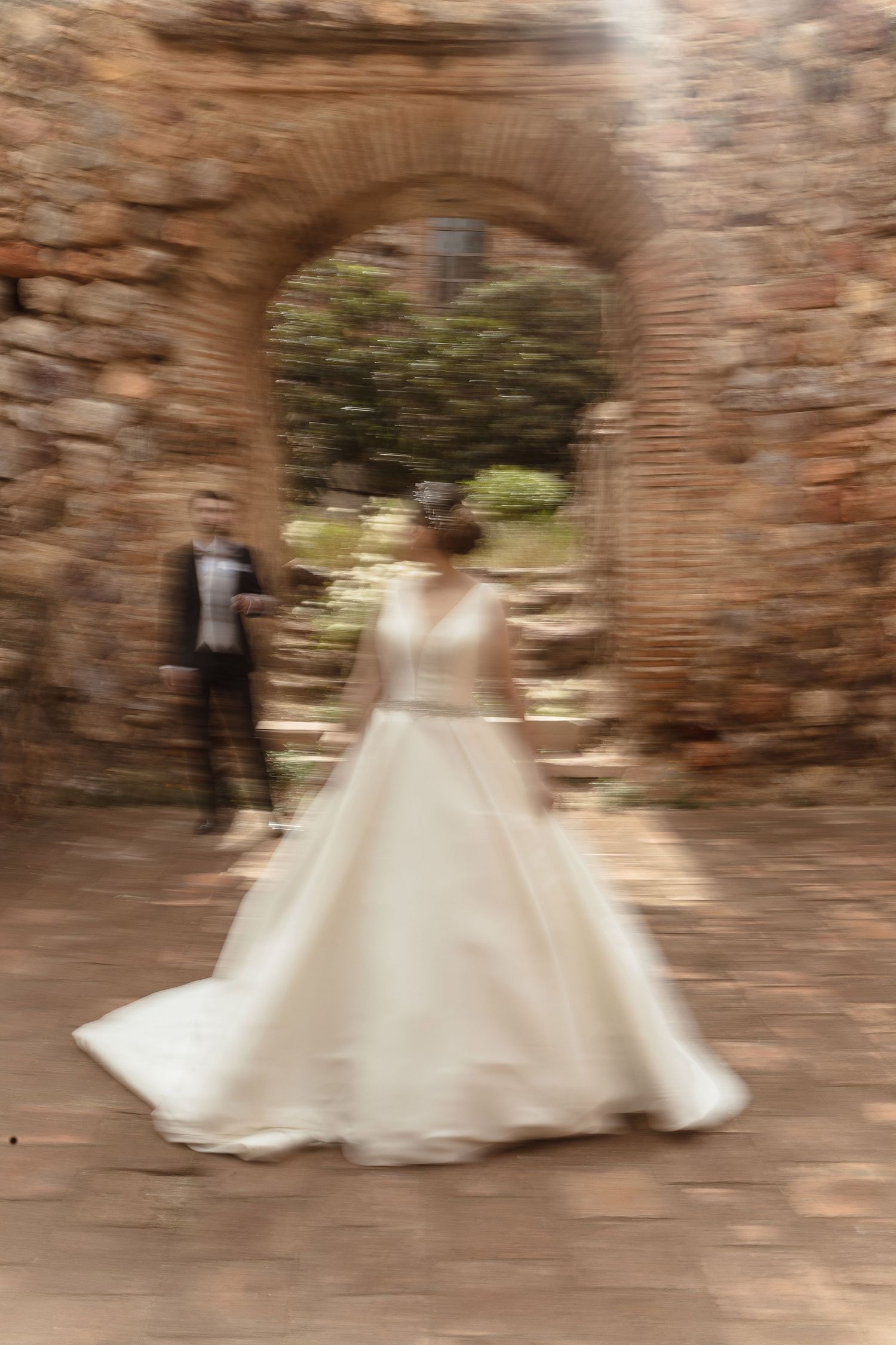 A dreamy motion-blurred photo of a wedding dress under a stone archway at a historic venue.