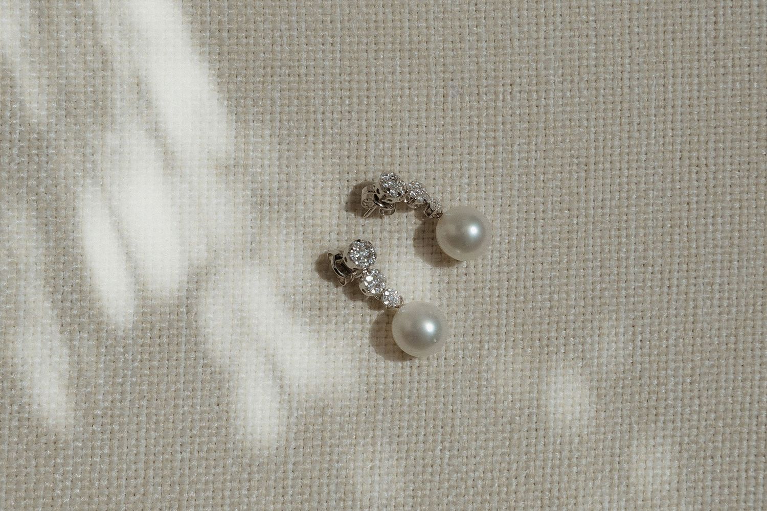 Delicate pearl and diamond stud earrings displayed on a textured white surface.