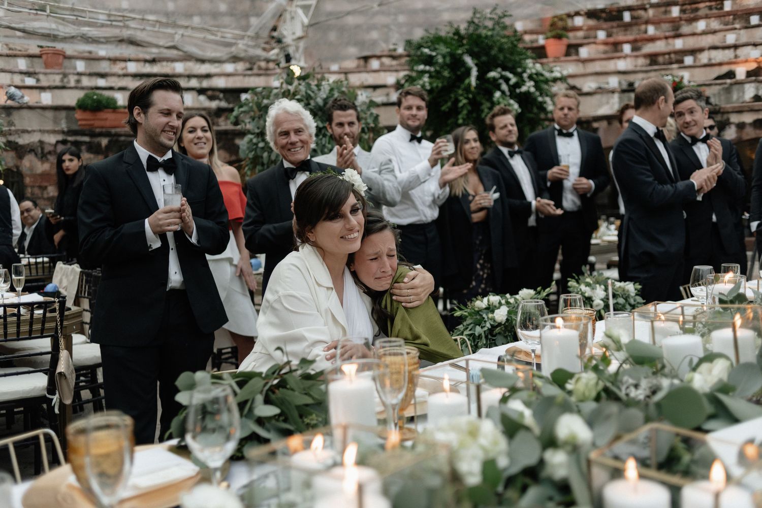 Elegant outdoor wedding reception at rustic brick venue with tables decorated in greenery and glassware.