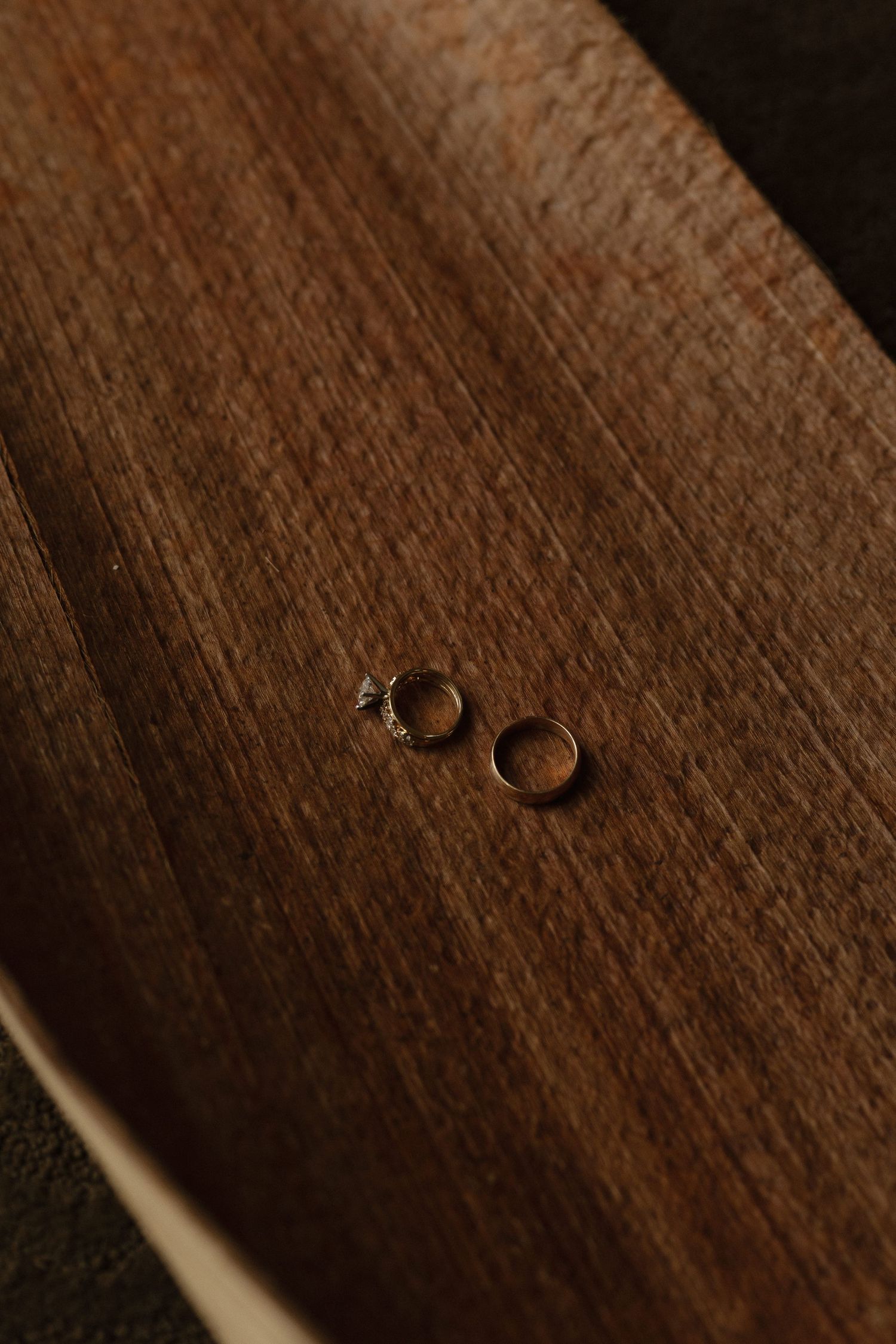 Wedding rings rest on a dark wooden surface casting subtle shadows in dramatic lighting.