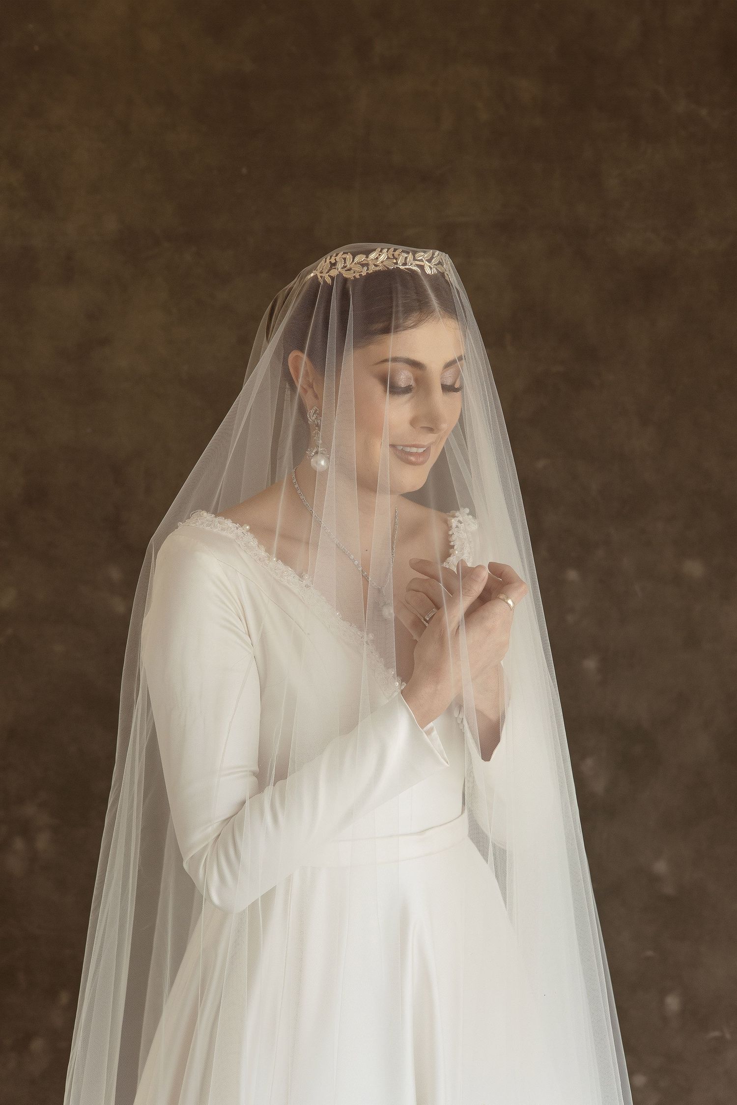 Bride in elegant long sleeve wedding dress and veil poses with closed eyes in dreamy vintage portrait.