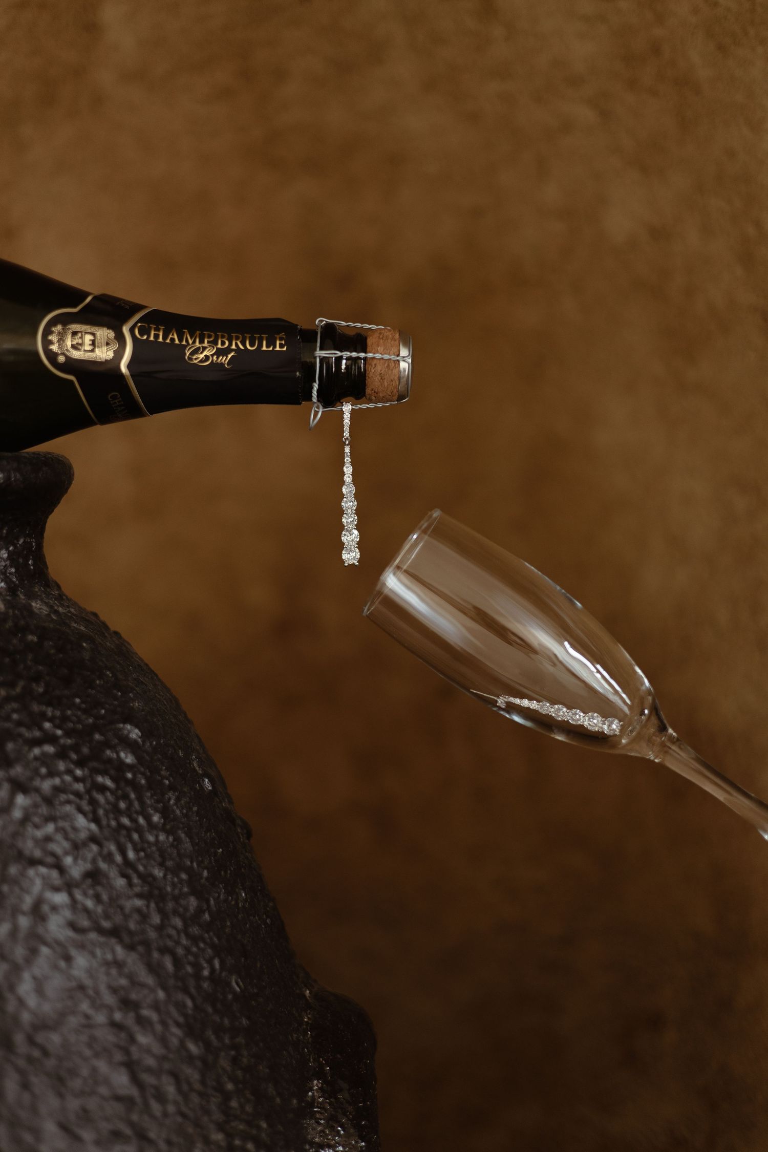 Champagne being poured from a bottle into an elegant glass flute against a dark brown background.