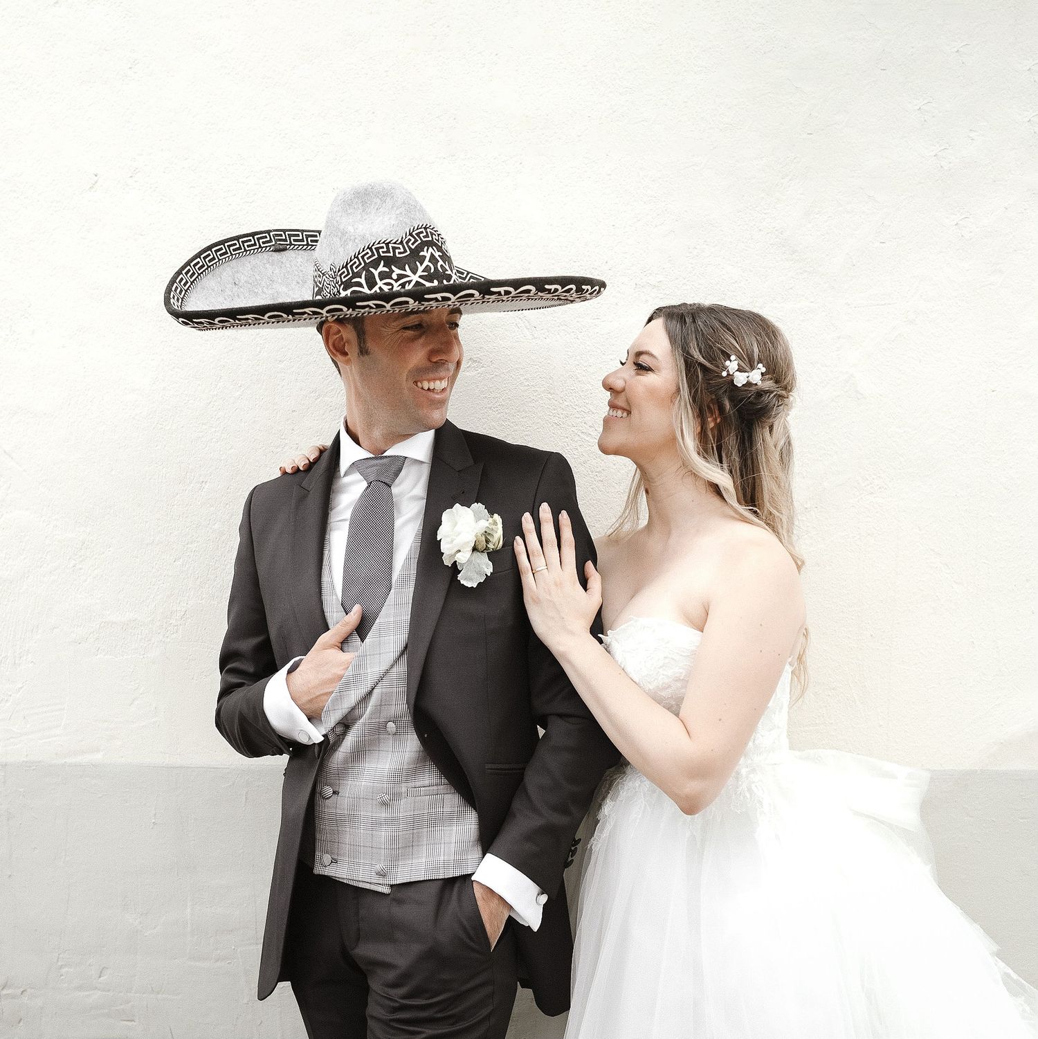 A romantic wedding couple poses together in formal attire against a light background.