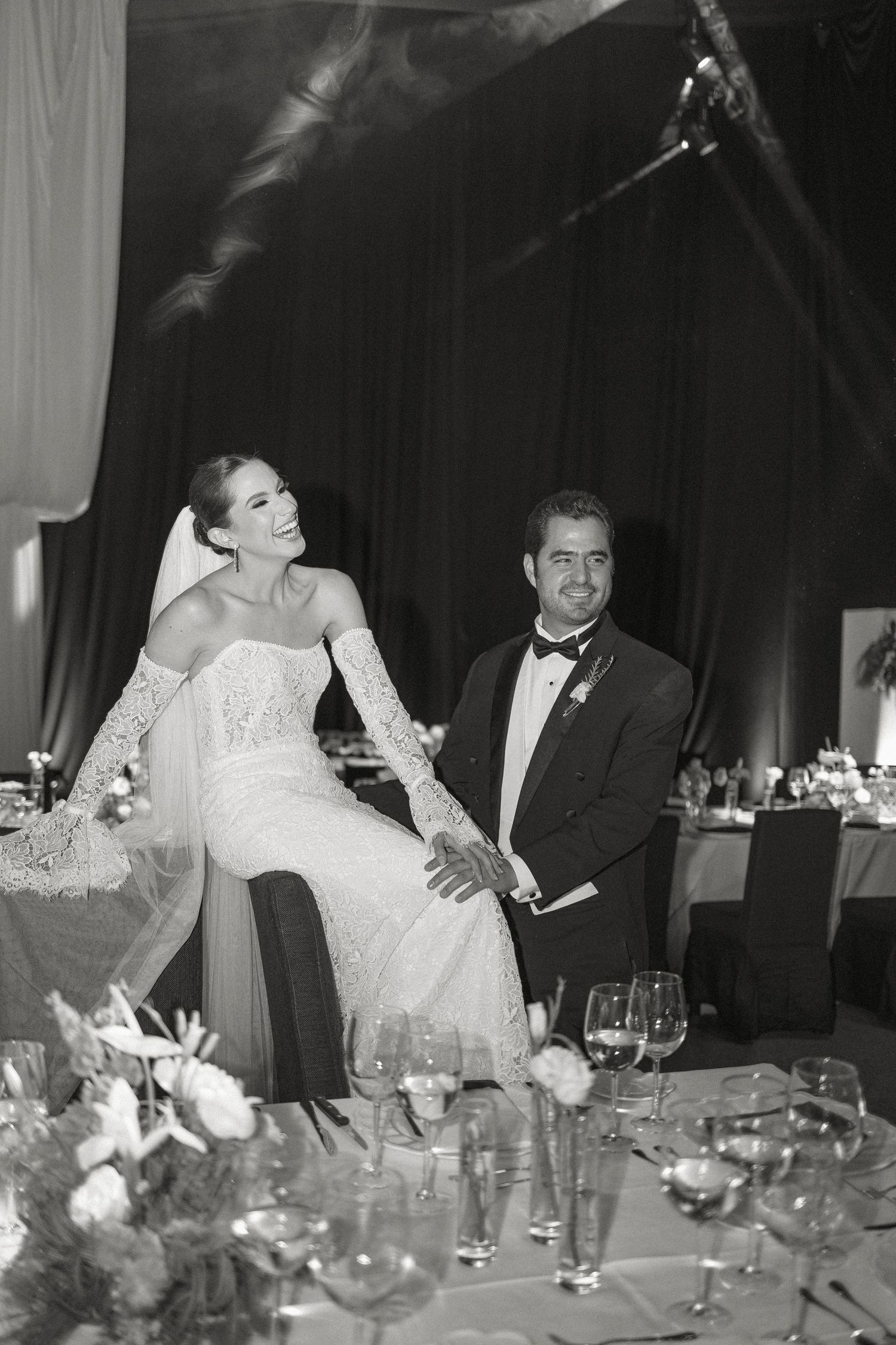 A series of black and white candid reception photos showing laughter and joy at an elegant dinner table setting.