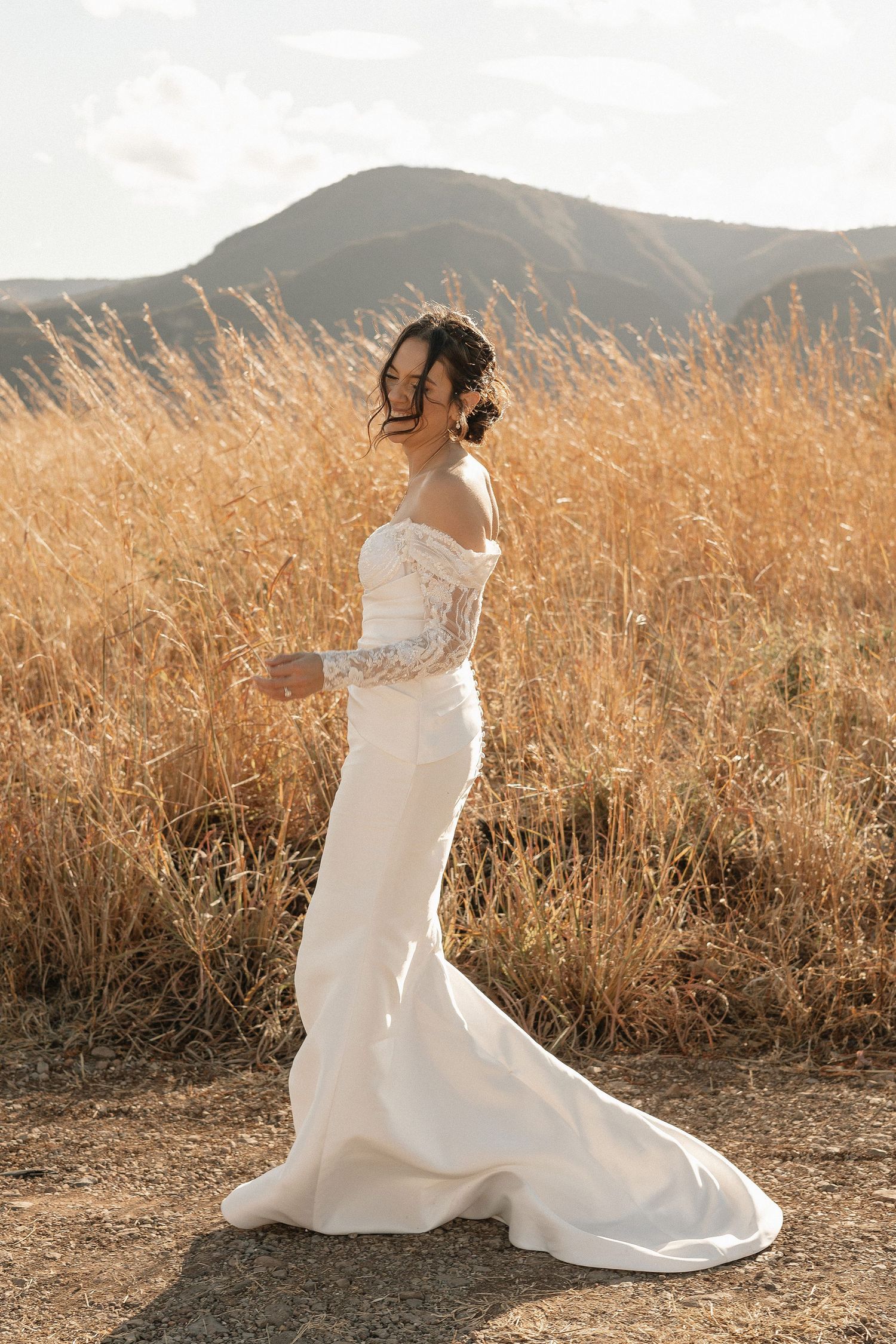 Ethereal bridal photos in white gown spinning through golden sunlit field with mountains in background.