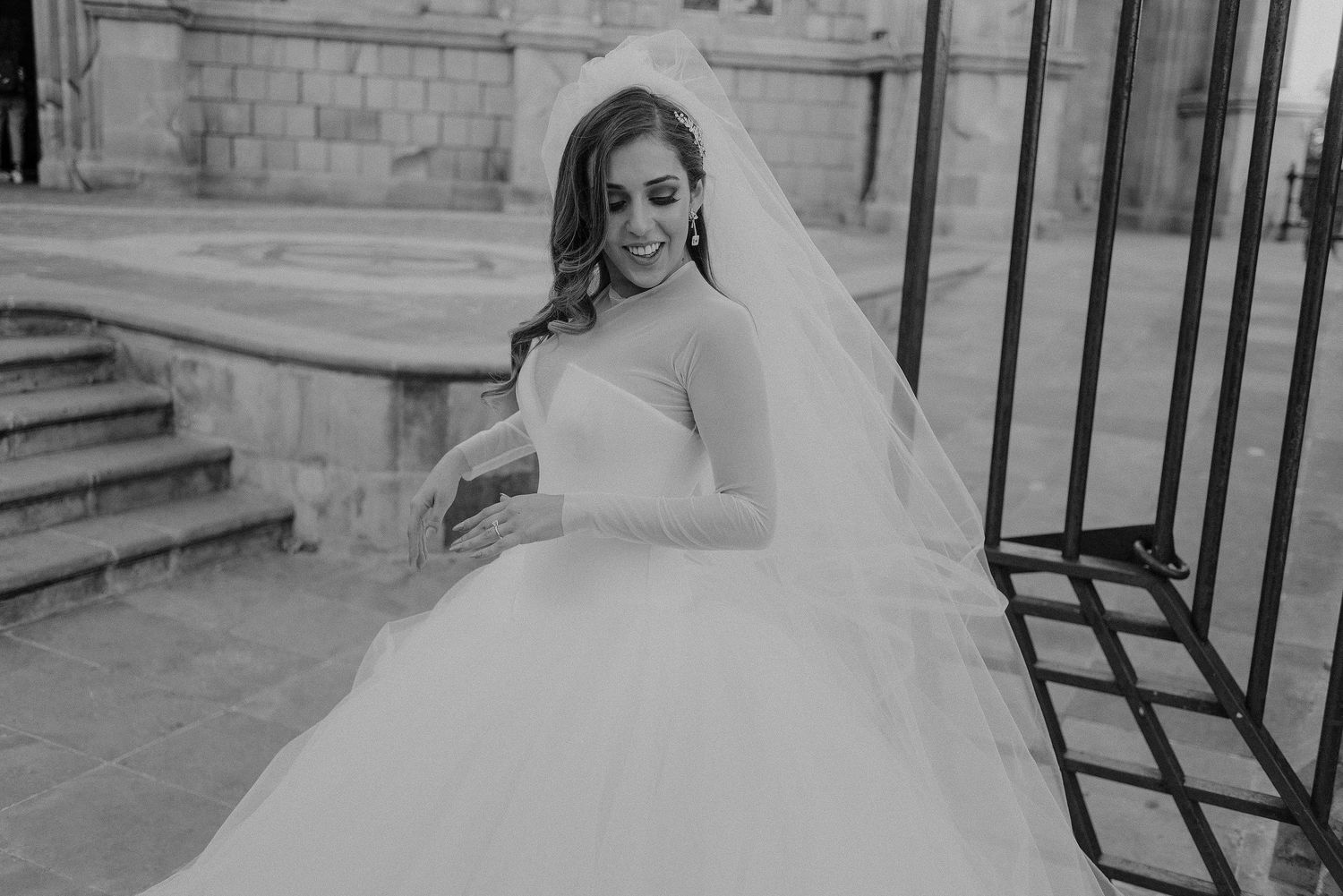 Black and white photo of bride in ballgown twirling on stone steps.