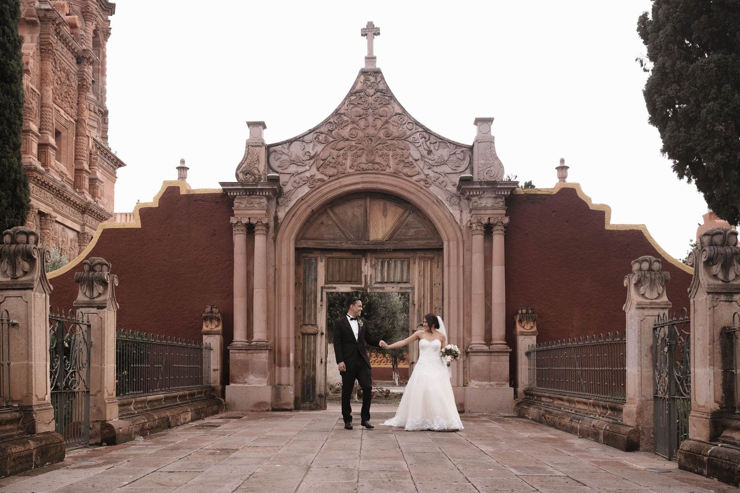 Newlyweds standing before ornate gothic church entrance with stone archway.