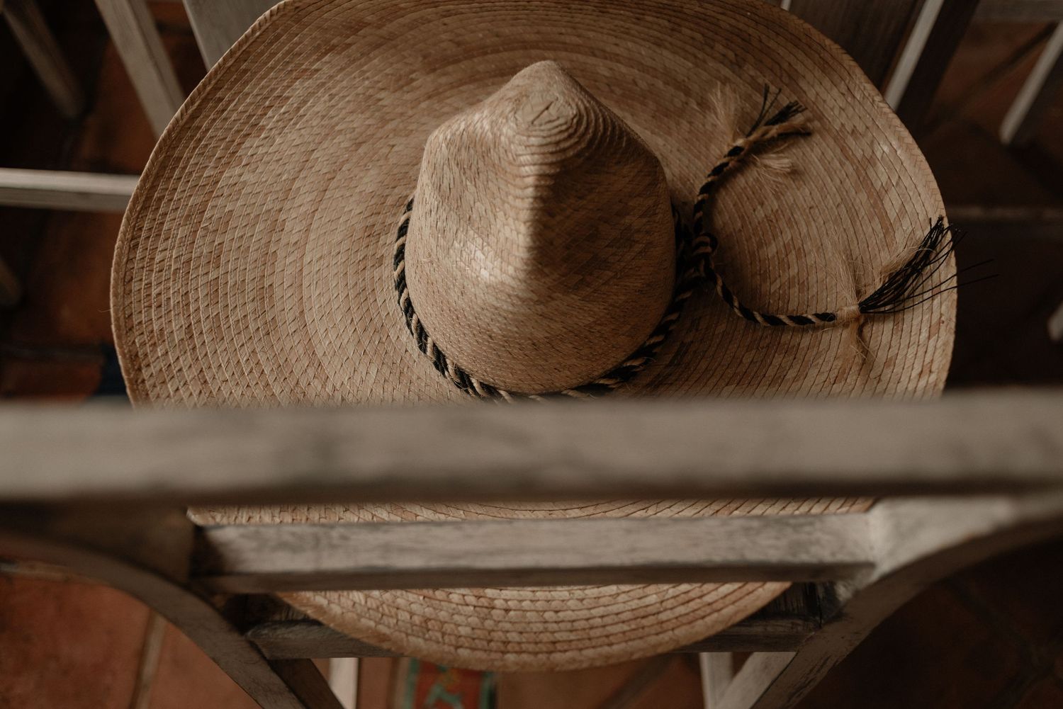 A rustic straw hat with braided detail sits on a wooden shelf in warm sepia tones.