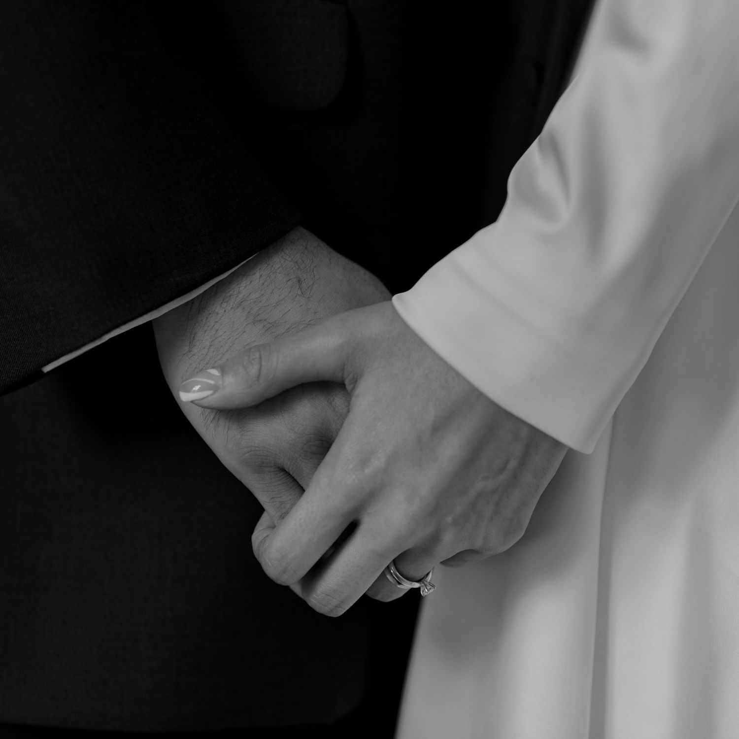 Close-up black and white photo of hands holding each other against a dark background.