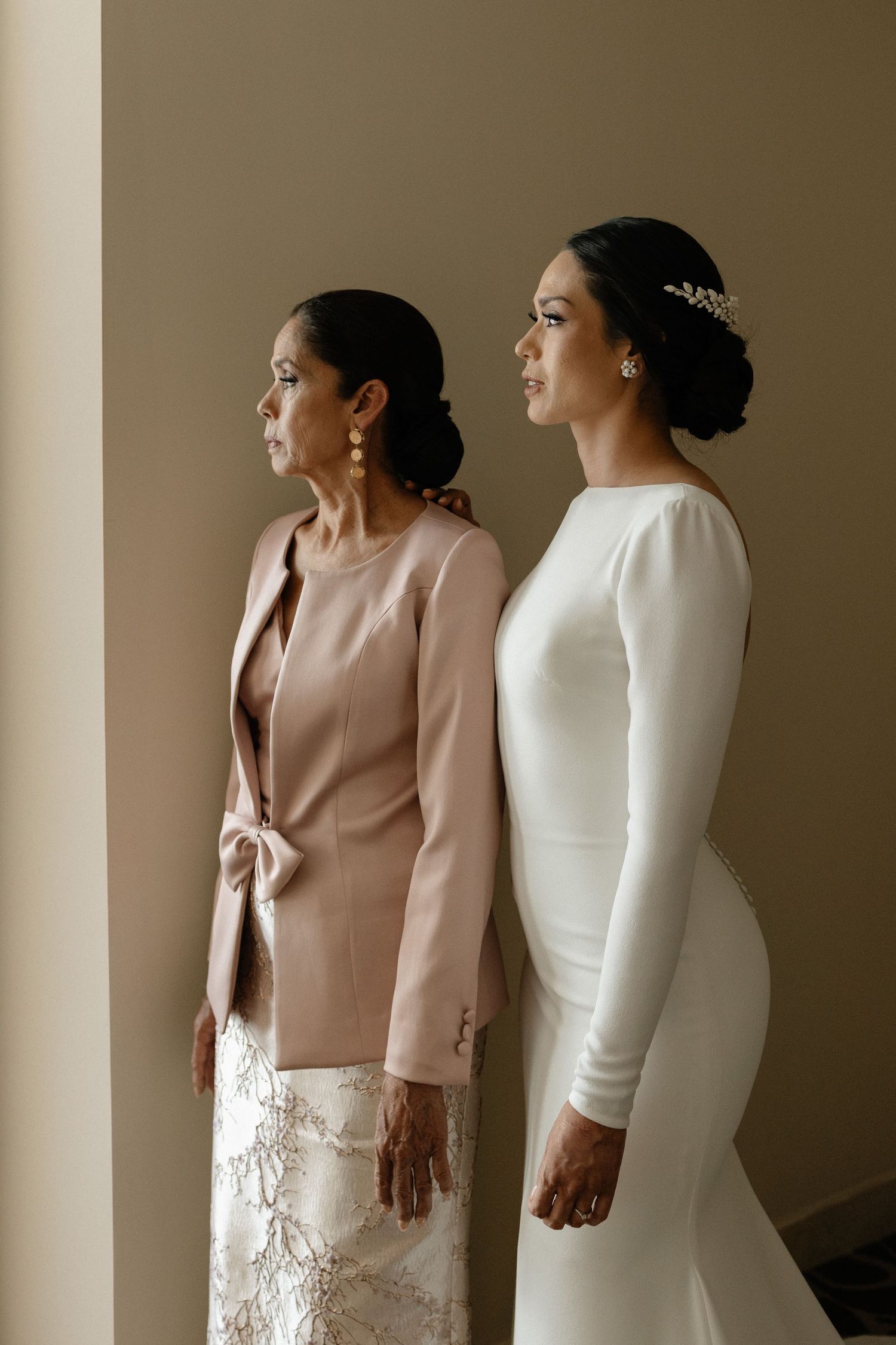 Two figures in elegant attire stand back-to-back in a minimalist setting with soft lighting and neutral tones.