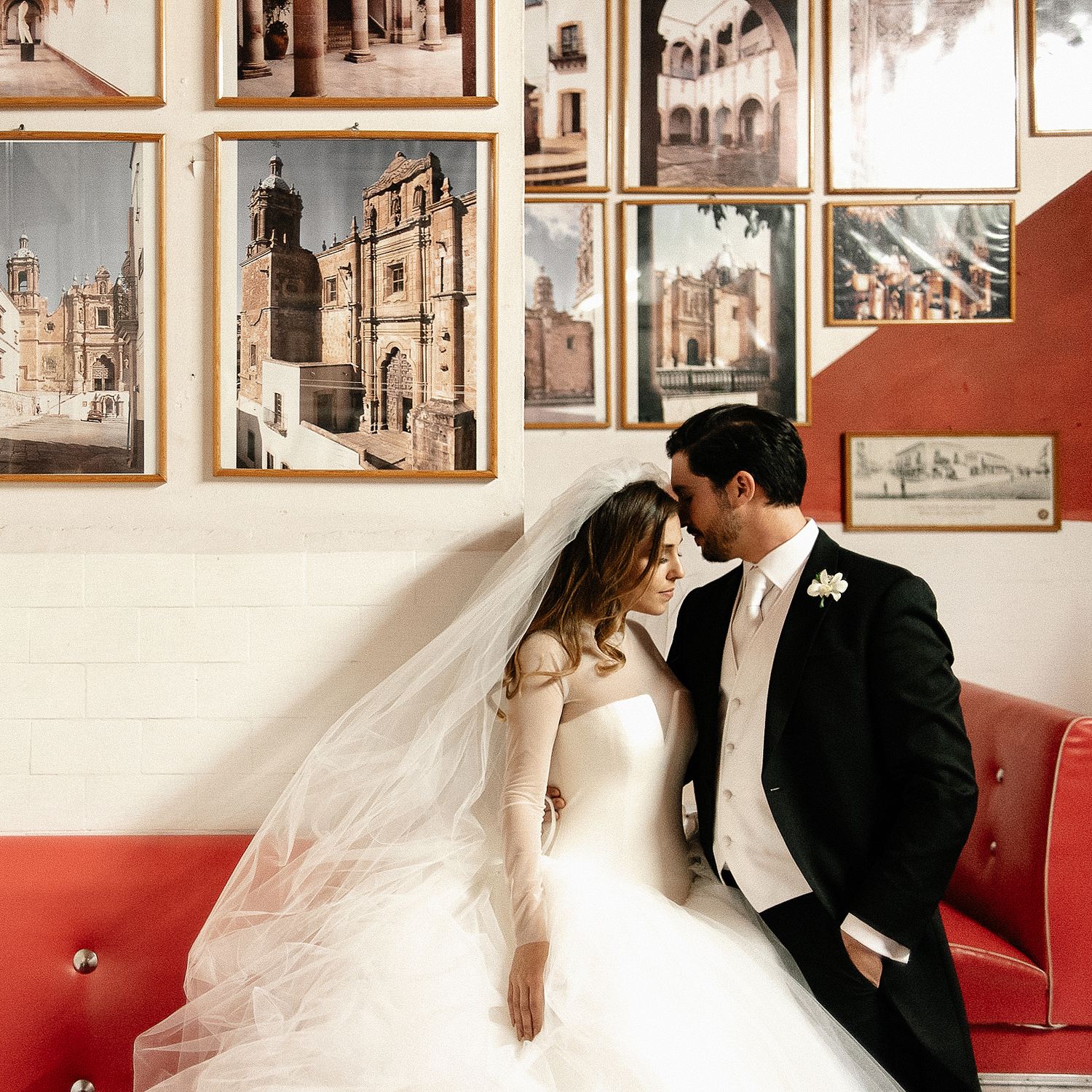 Wedding couple poses against wall decorated with vintage photographs.
