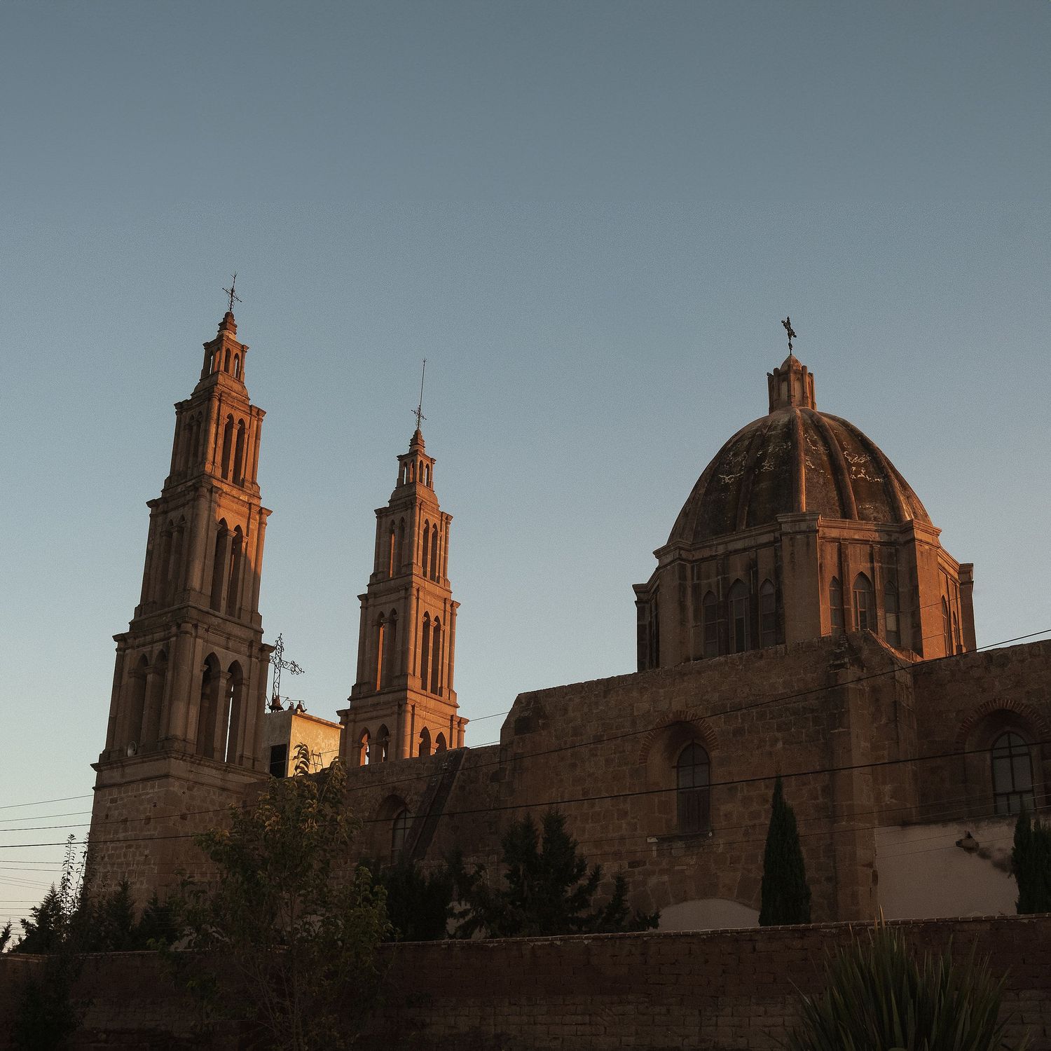 Historic cathedral with twin towers and dome against a dusky blue sky.