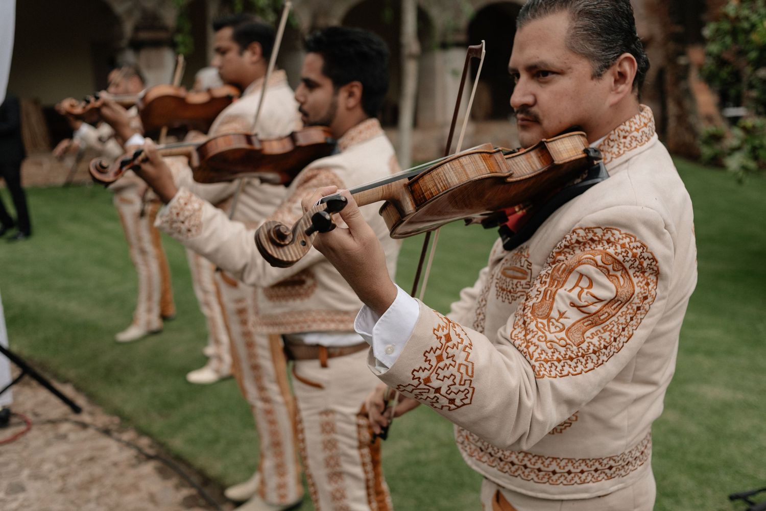 Musicians in traditional Mexican mariachi outfits perform with violins at an outdoor event.
