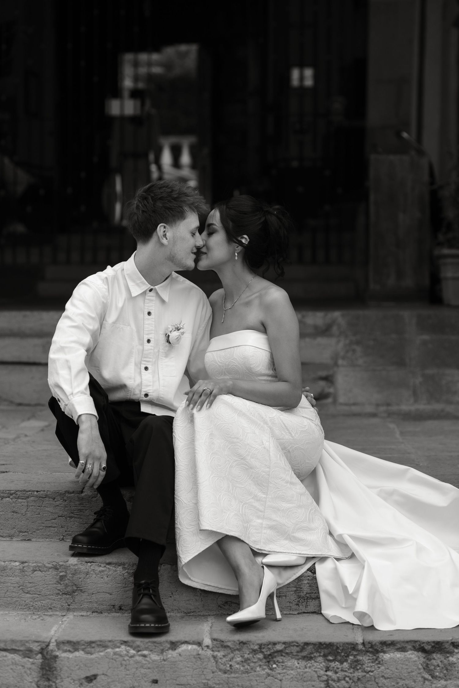 Black and white wedding photo series showing romantic couple sitting together on steps in formal attire.