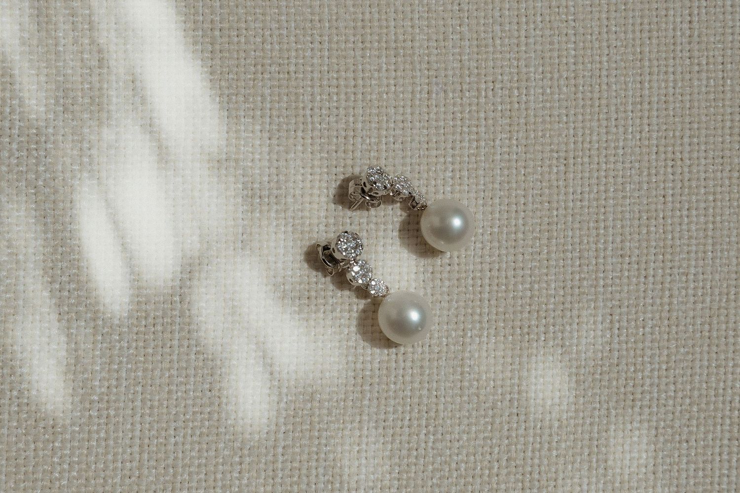 Pearl and crystal wedding jewelry details photographed on textured linen background.