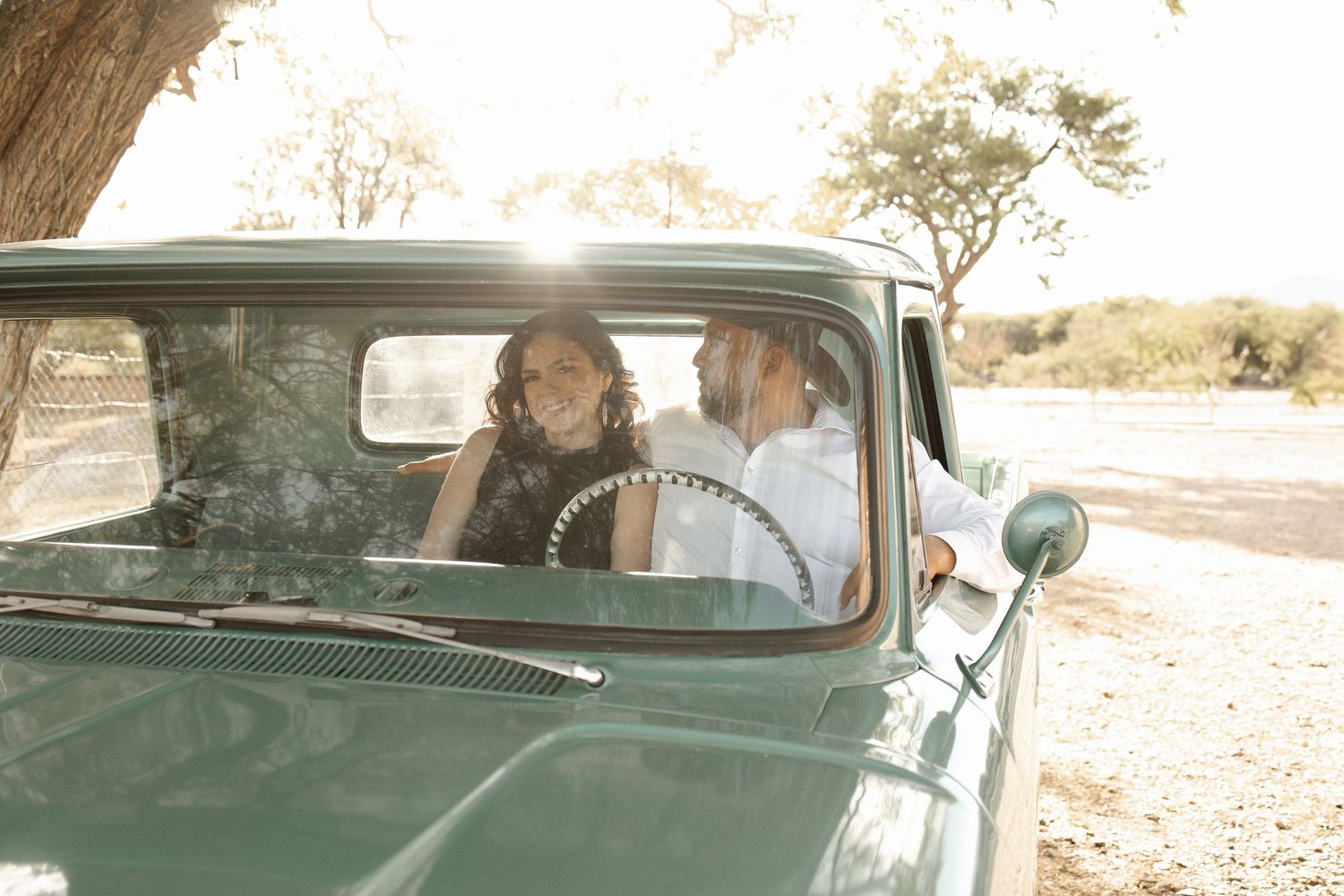 A vintage green car parked on a dirt road at sunset with sunlight streaming through the windshield.