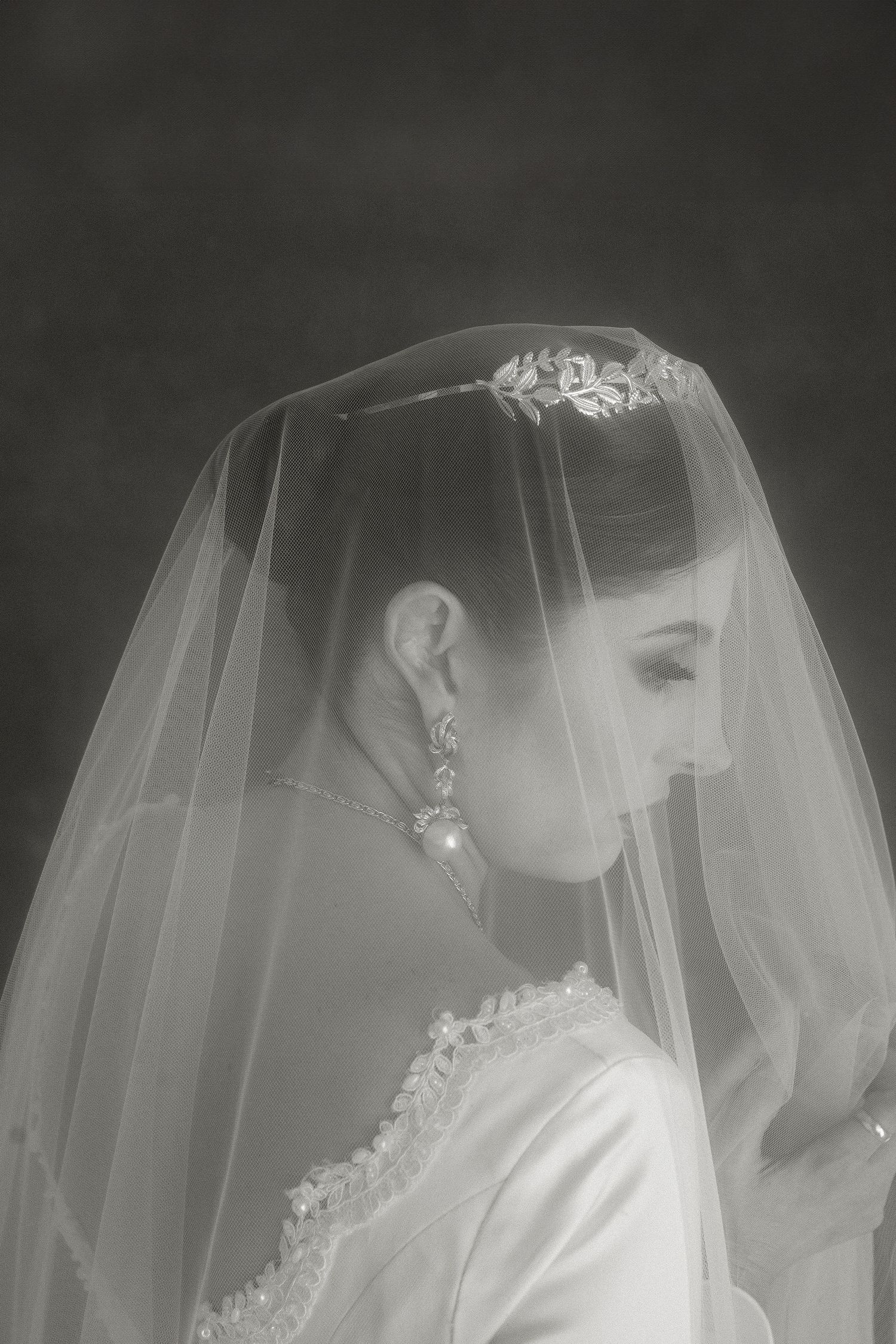 A black and white bridal portrait showing a side profile with delicate veil and dangling earrings.