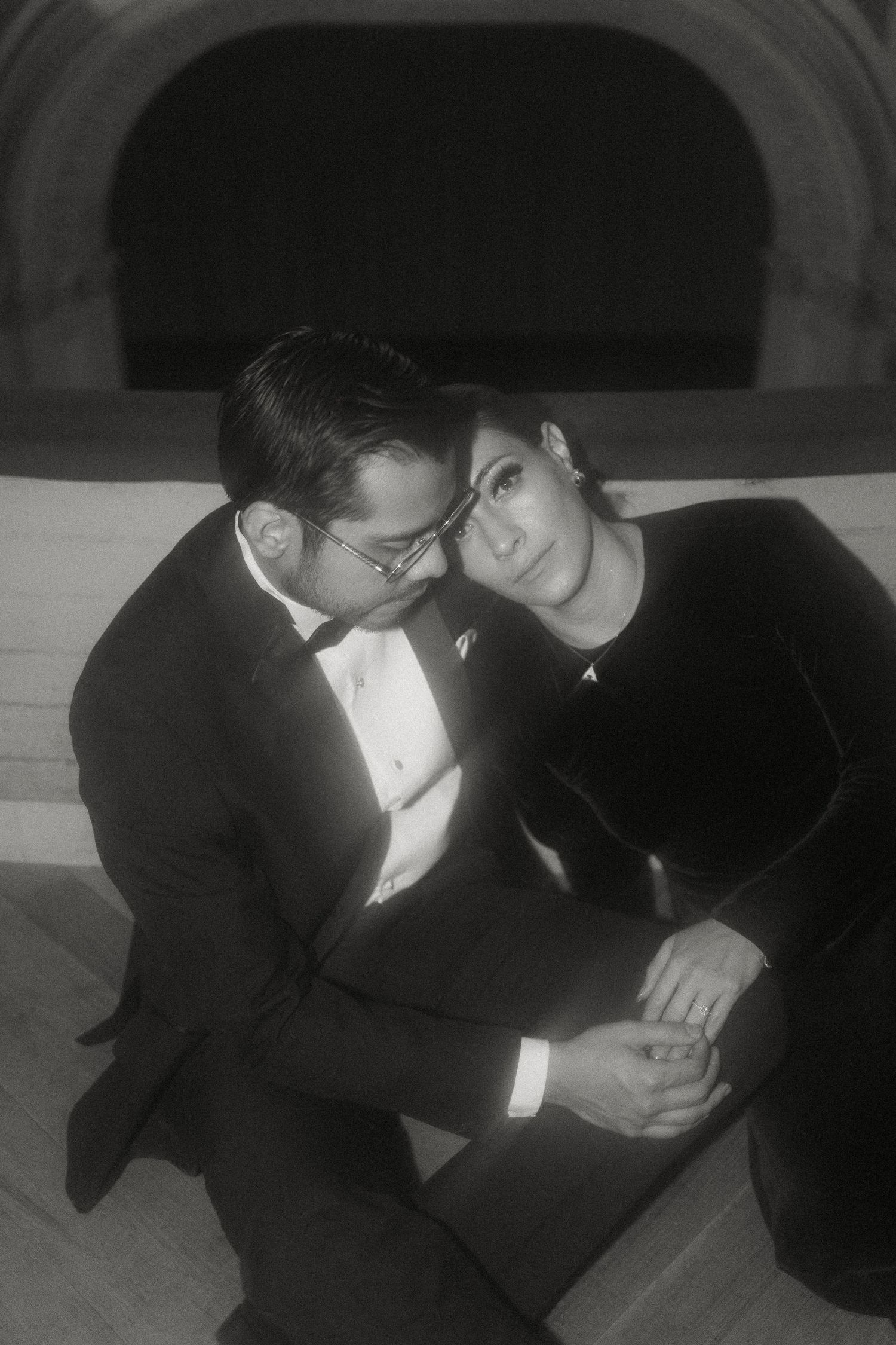 A romantic black and white photograph of a couple in formal attire sitting close together in an intimate moment.