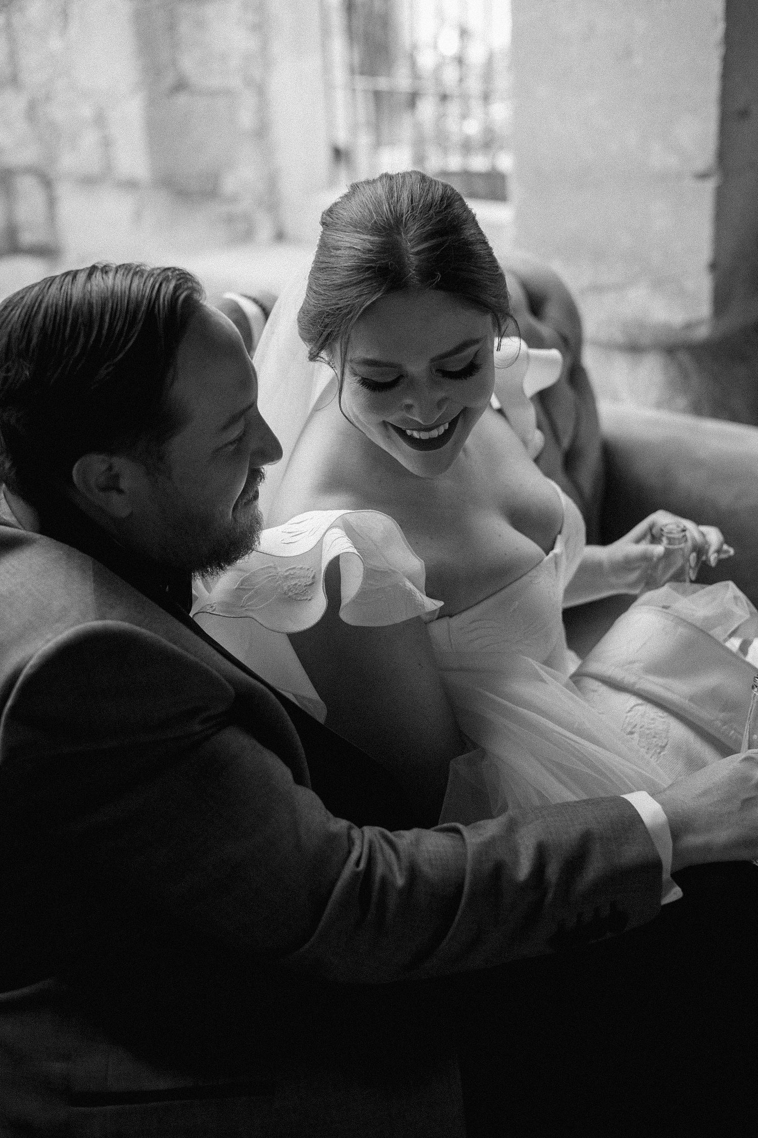 A tender black and white moment between newlyweds sharing laughter on their wedding day.