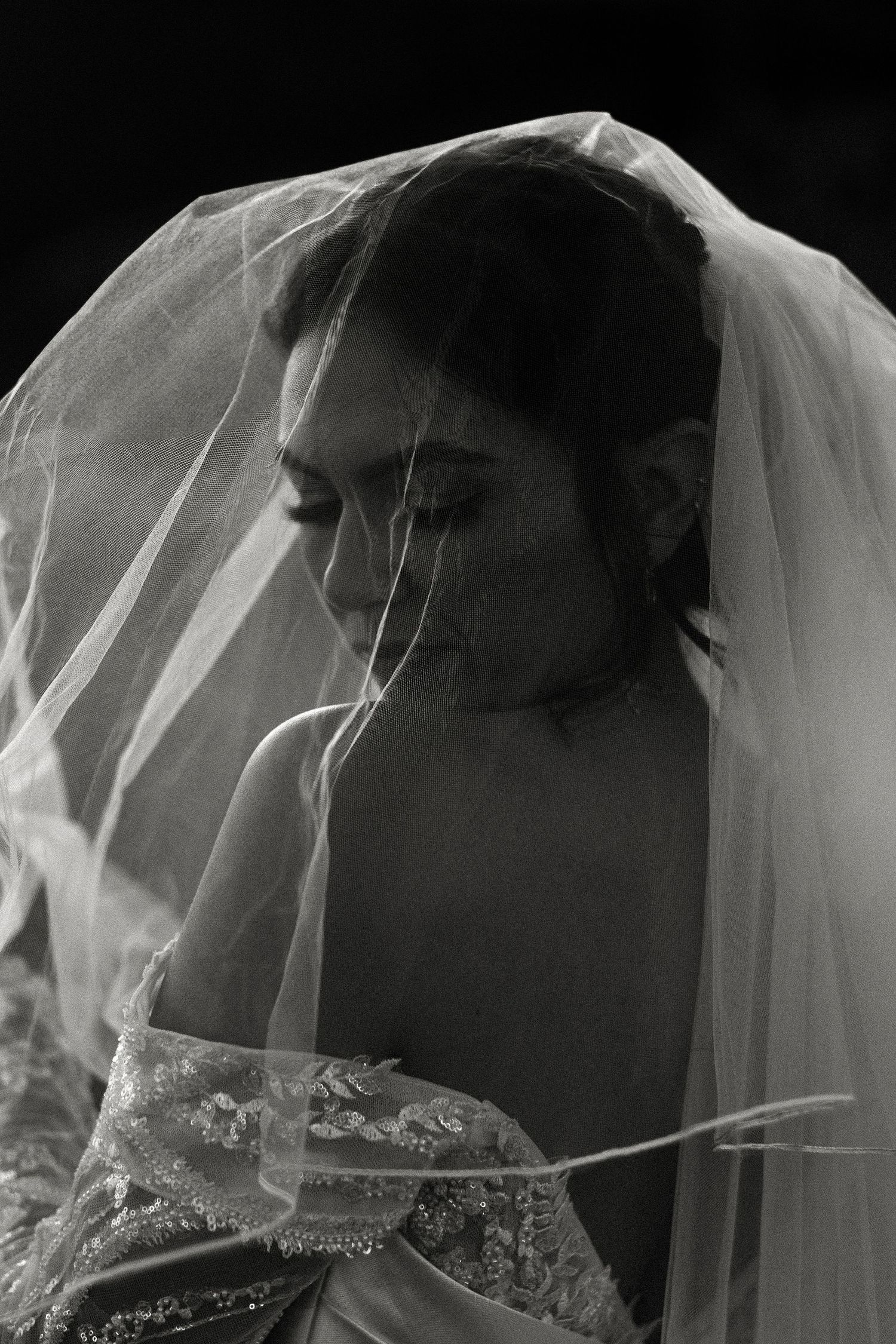 Dramatic black and white portrait through delicate bridal veil detail.