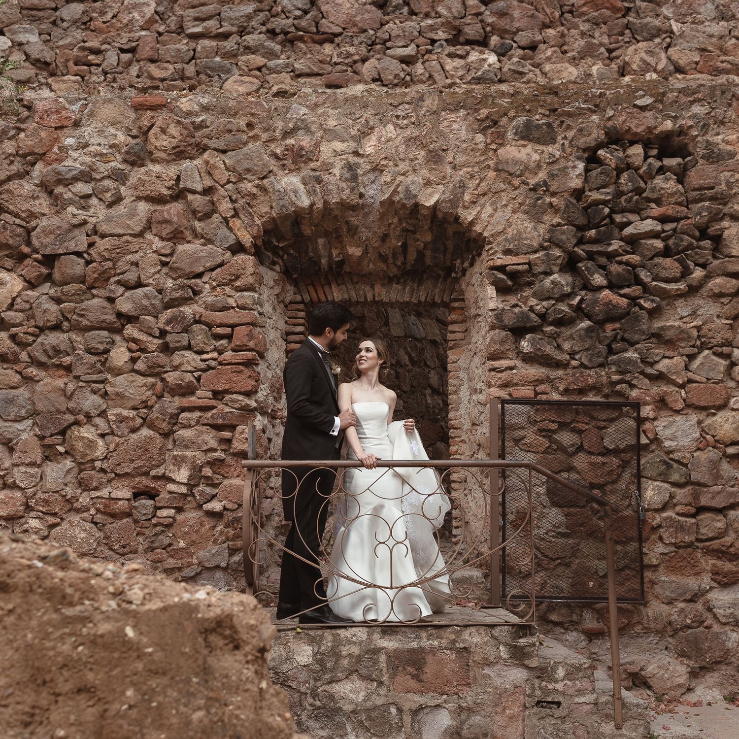 A romantic wedding scene framed within an ancient stone archway.