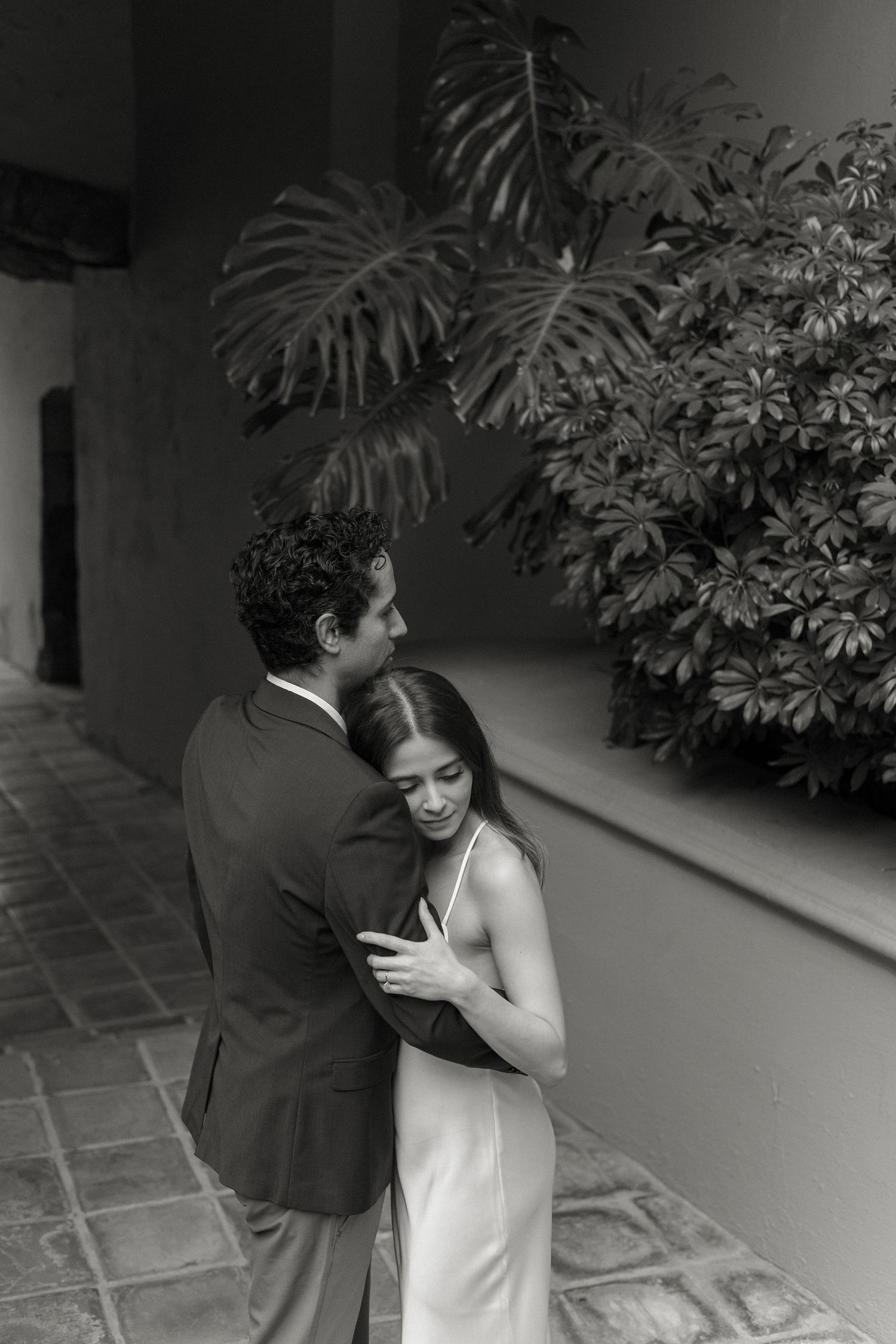 Couple embracing in a garden walkway with lush tropical plants and stone pavers.