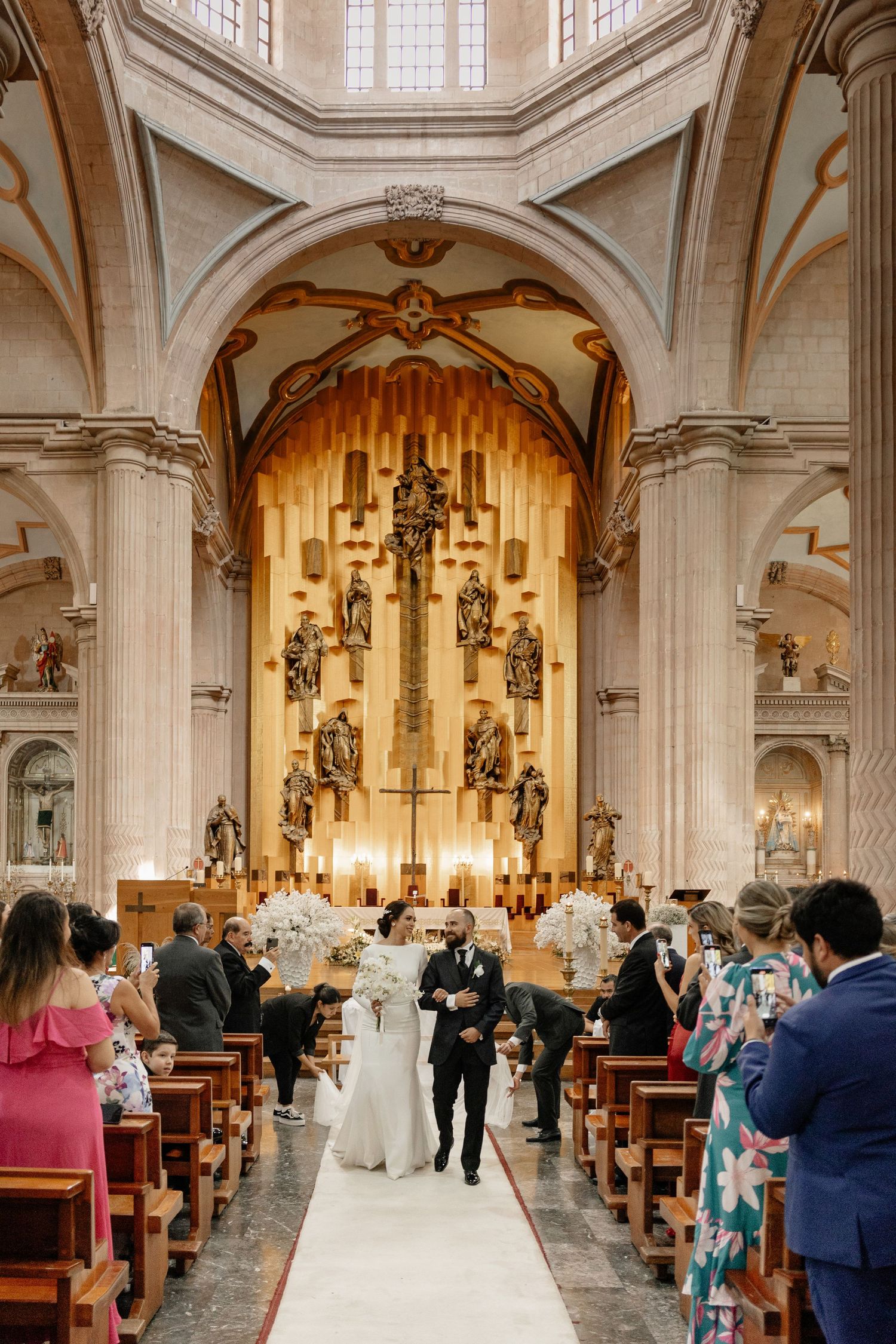 Interior view of a traditional church wedding ceremony with guests seated in wooden pews and ornate architectural details.