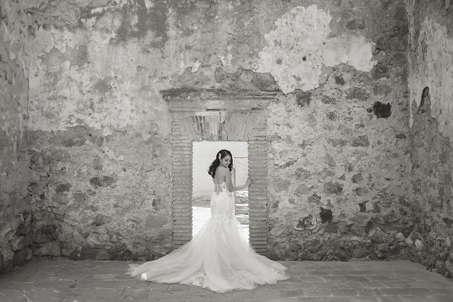 A series of elegant bridal portraits showing a flowing white wedding gown against rustic stone walls in natural light.