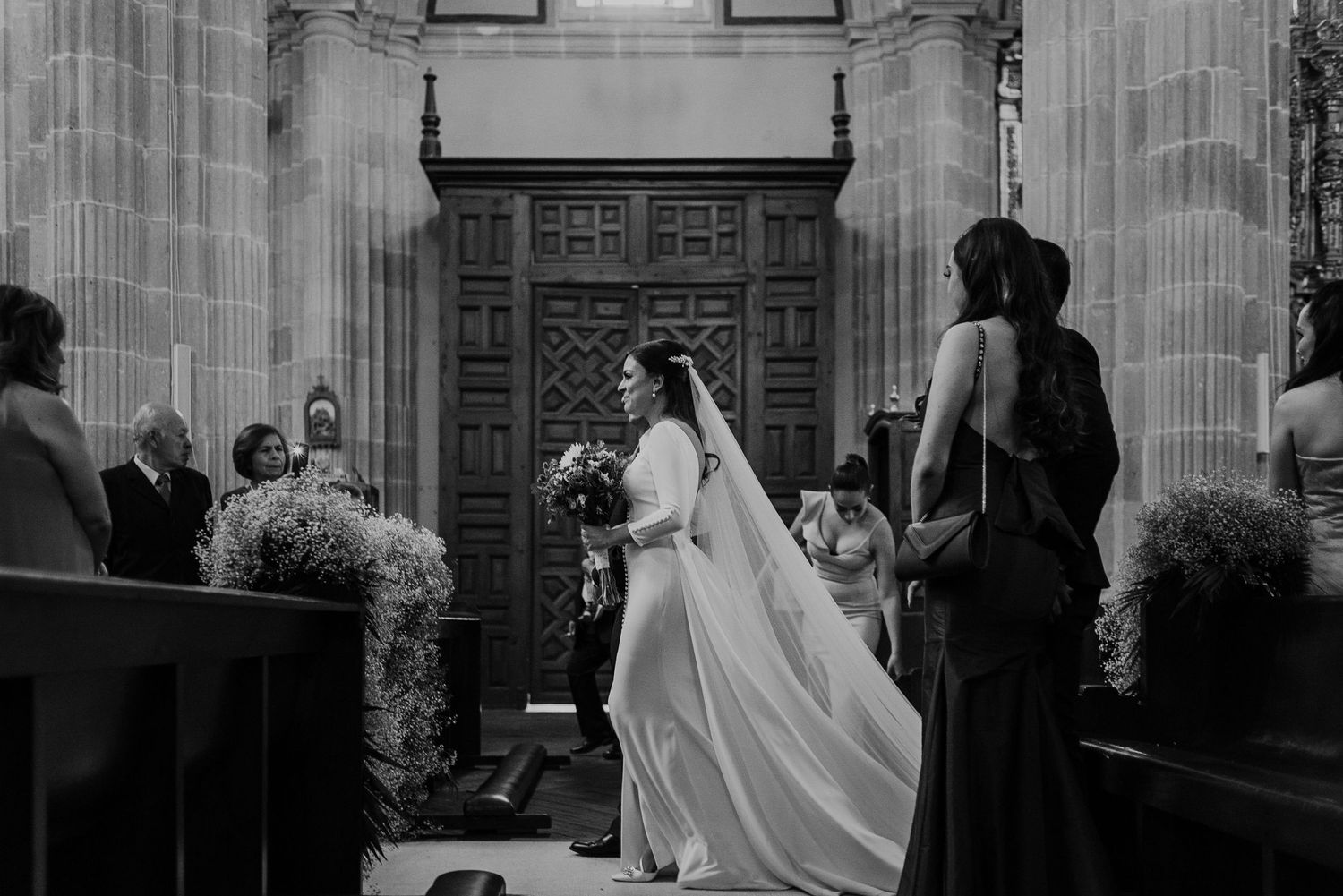 Black and white photograph of a traditional church wedding ceremony with architectural columns and wooden details.